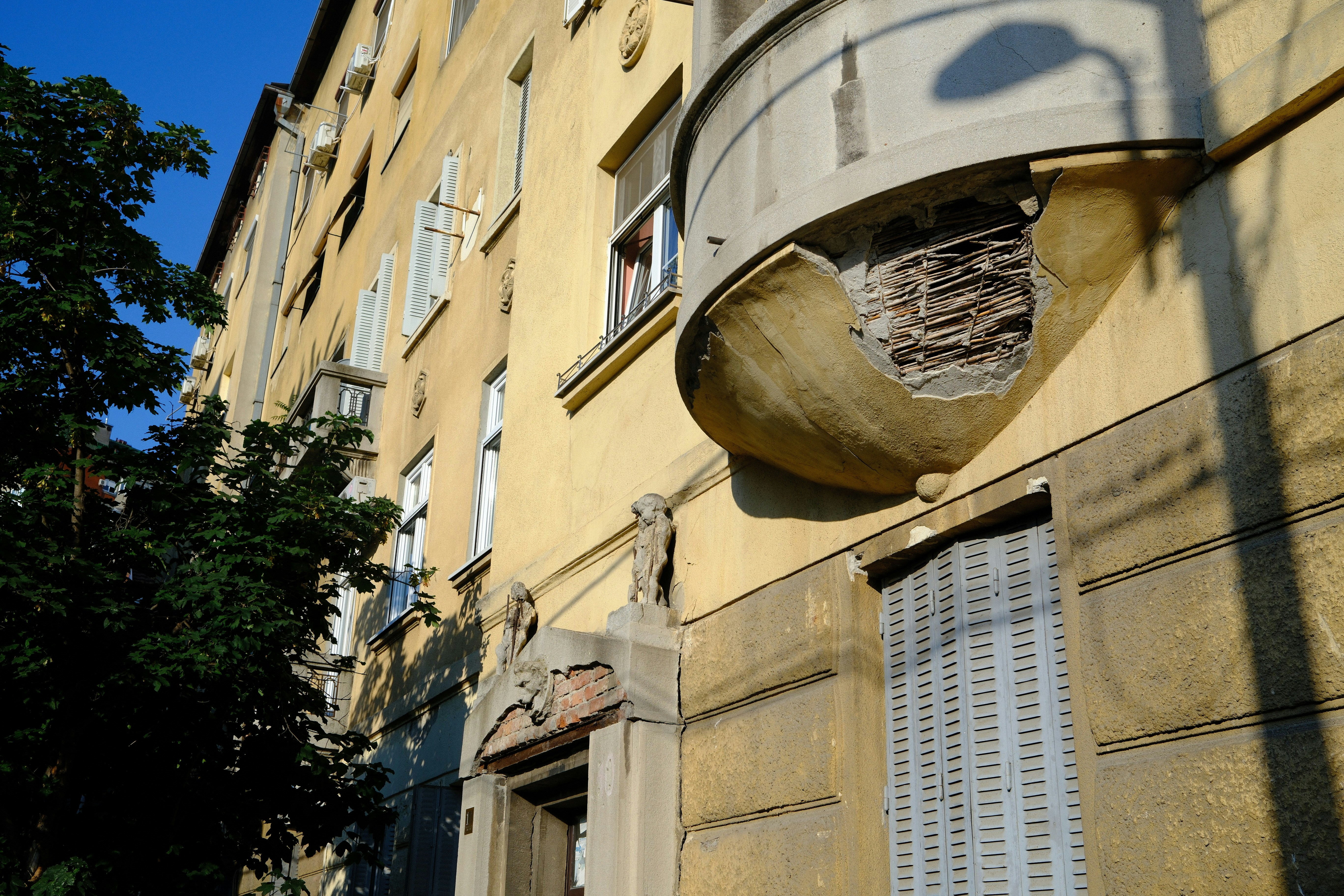 A yellow building with a unique, decorative balcony and trees.