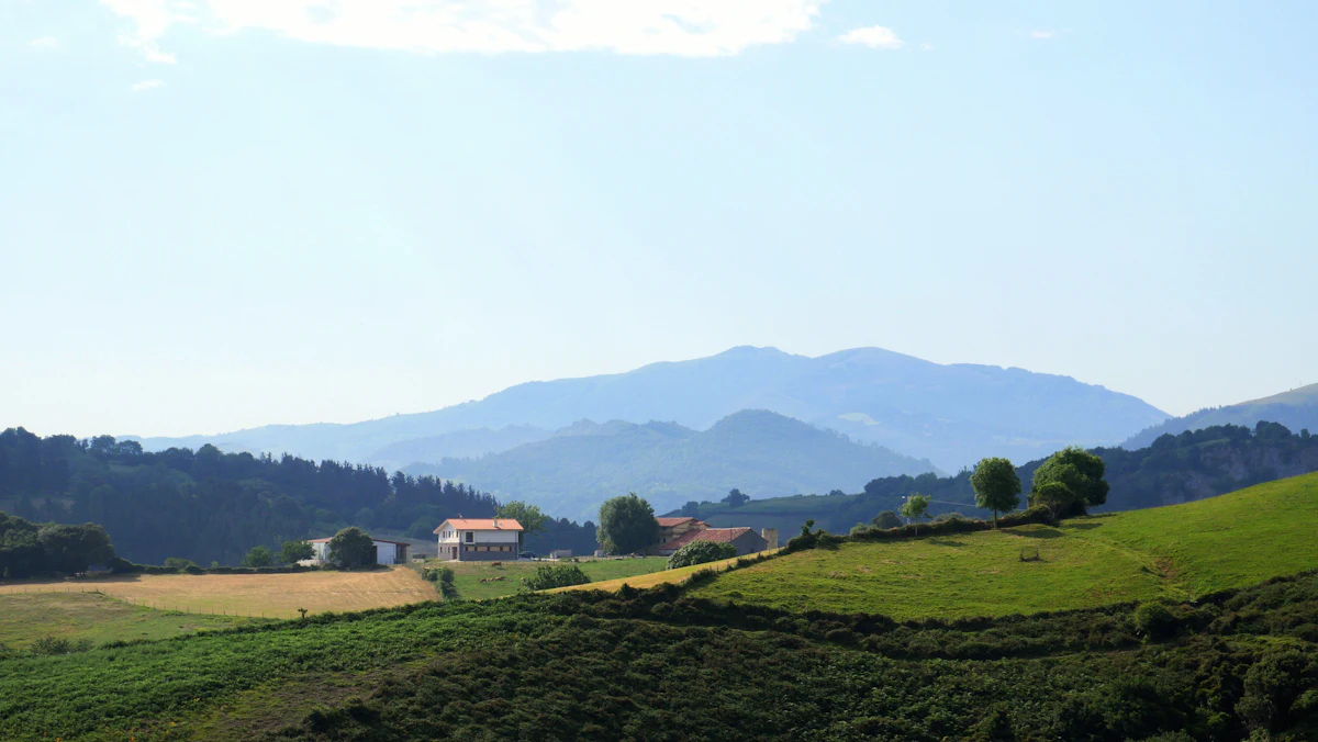 Green fields and white farmhouses in the Basque Country, with blue mountains behind