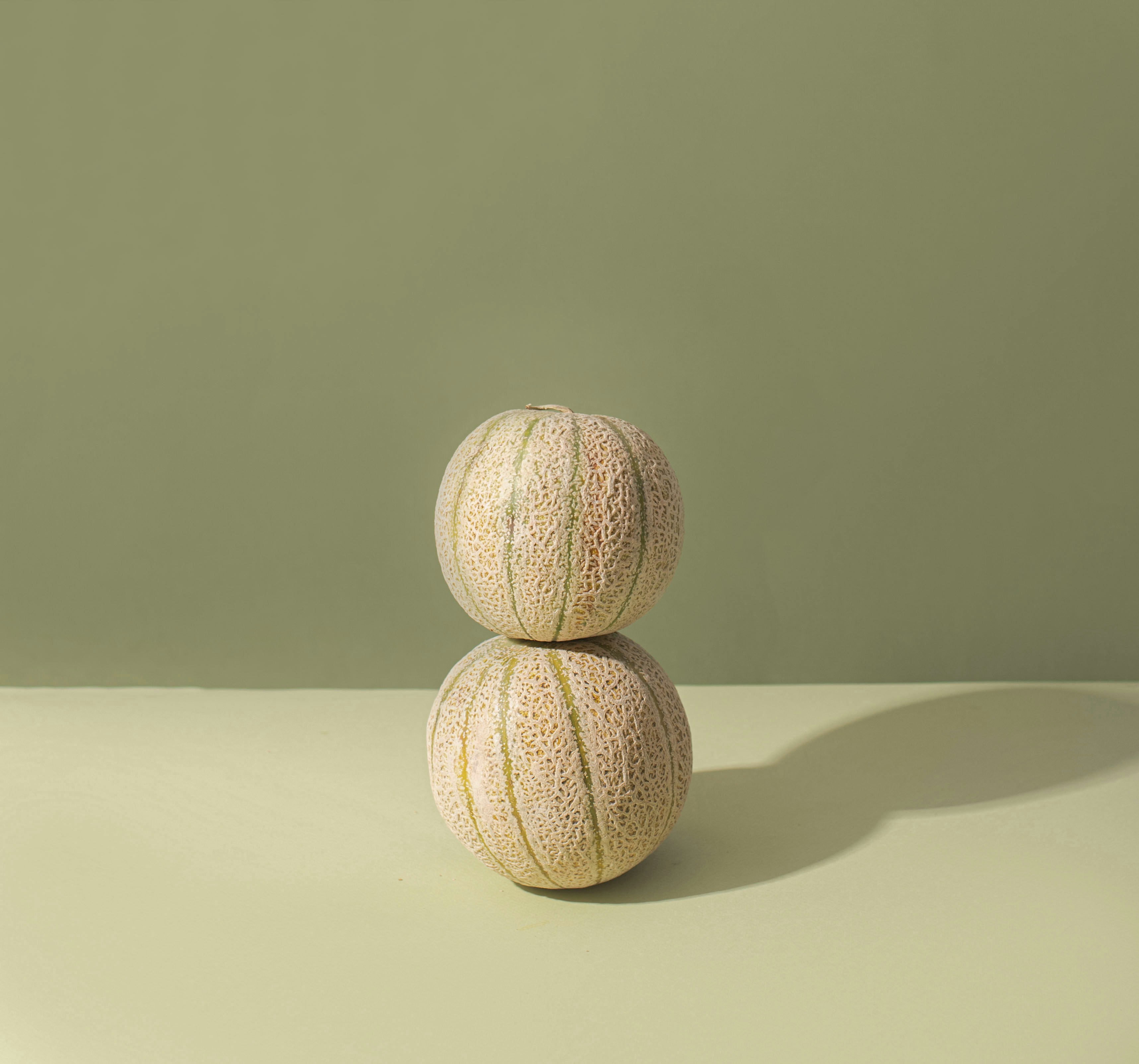 Two small, ribbed melons stacked on a green surface.
