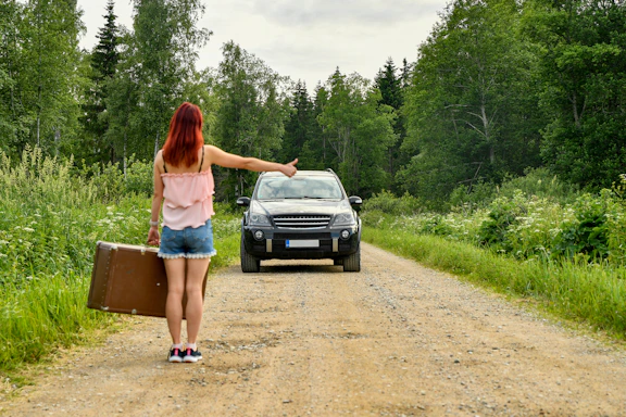 Red-haired woman hitchhiking with a suitcase on a dirt road