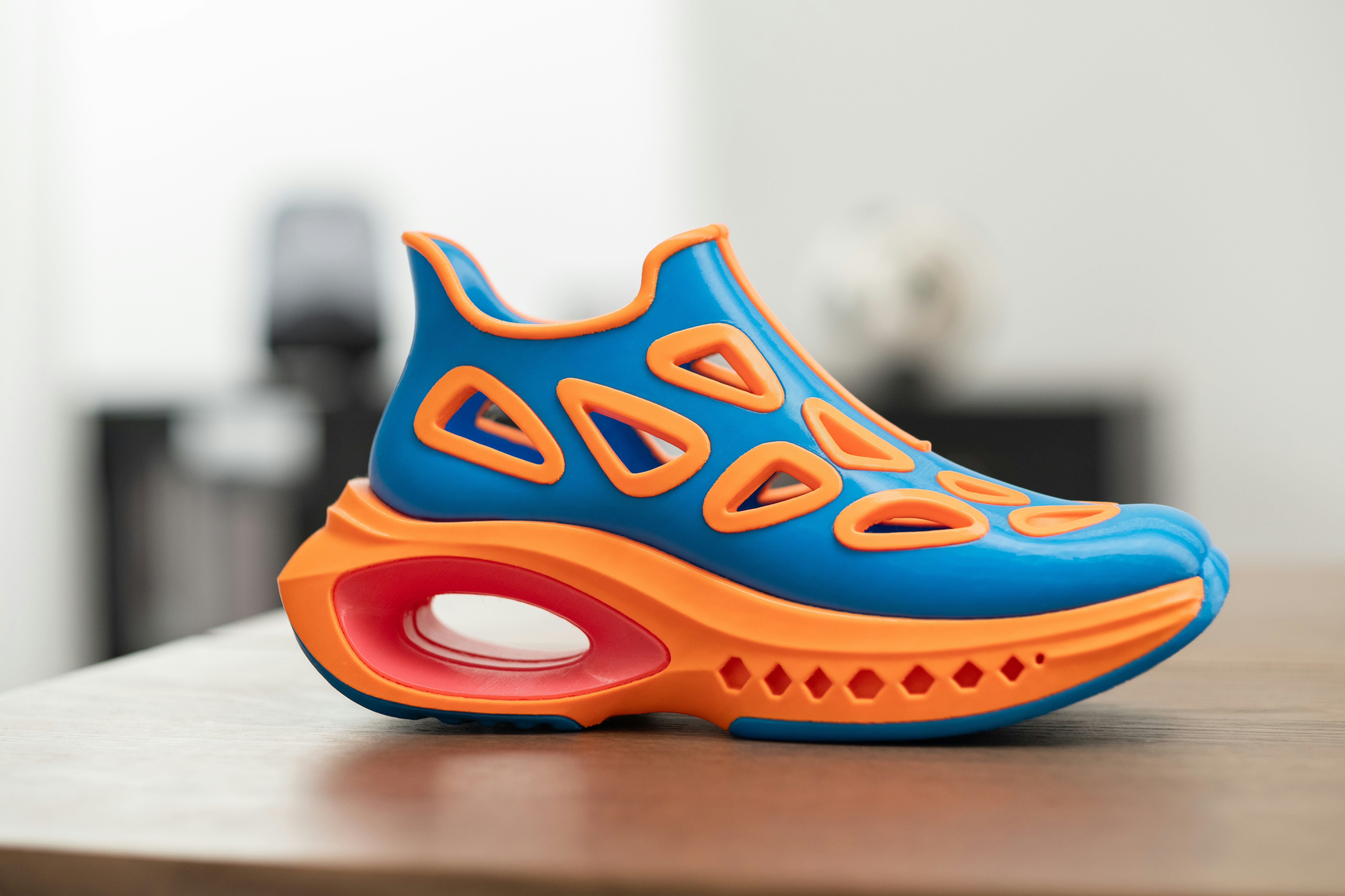 Ein leuchtend blauer und orangefarbener futuristischer Schuh auf einem Holztisch.