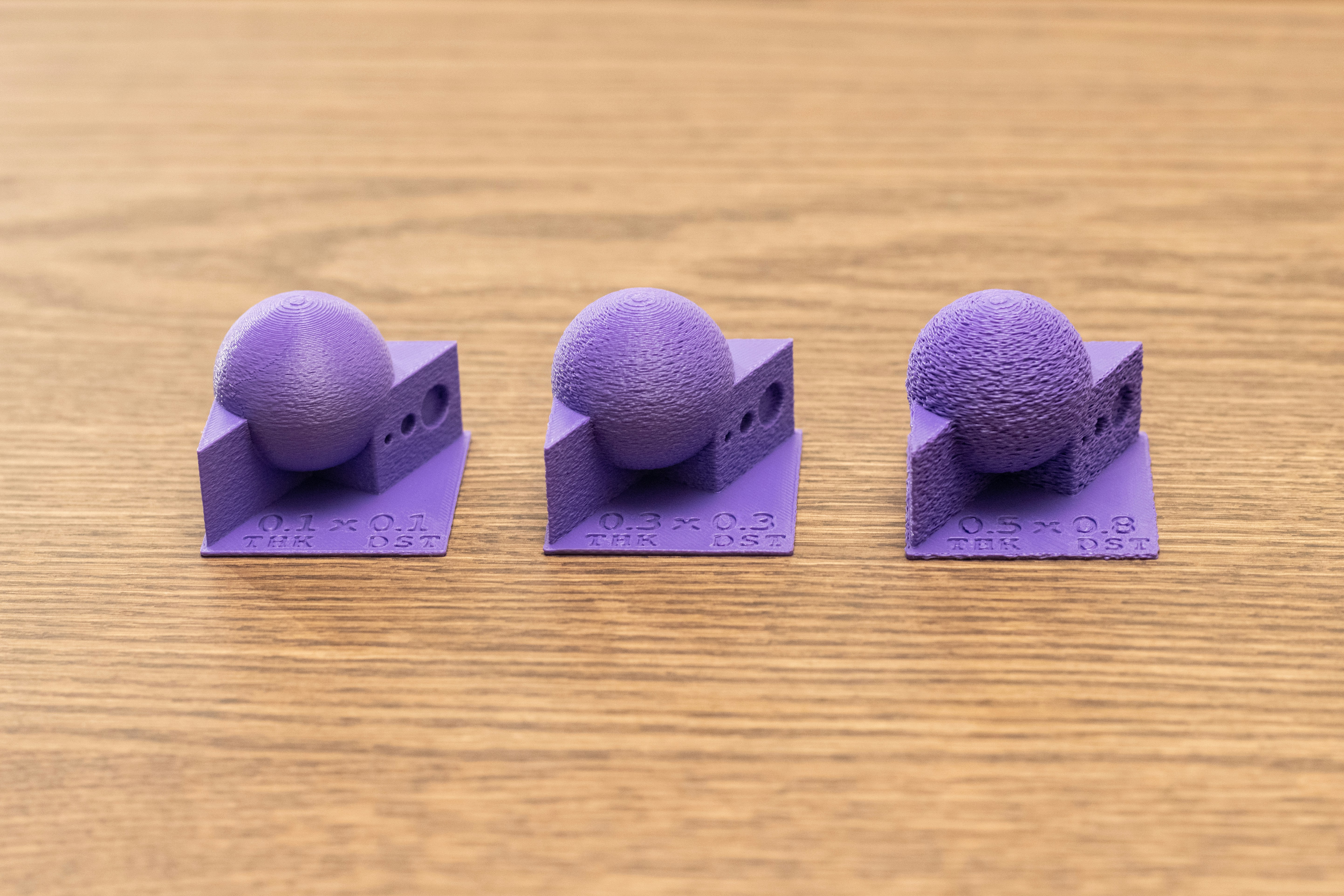Drei lila, 3D-gedruckte, strukturierte Kugeln auf einer Holzoberfläche.