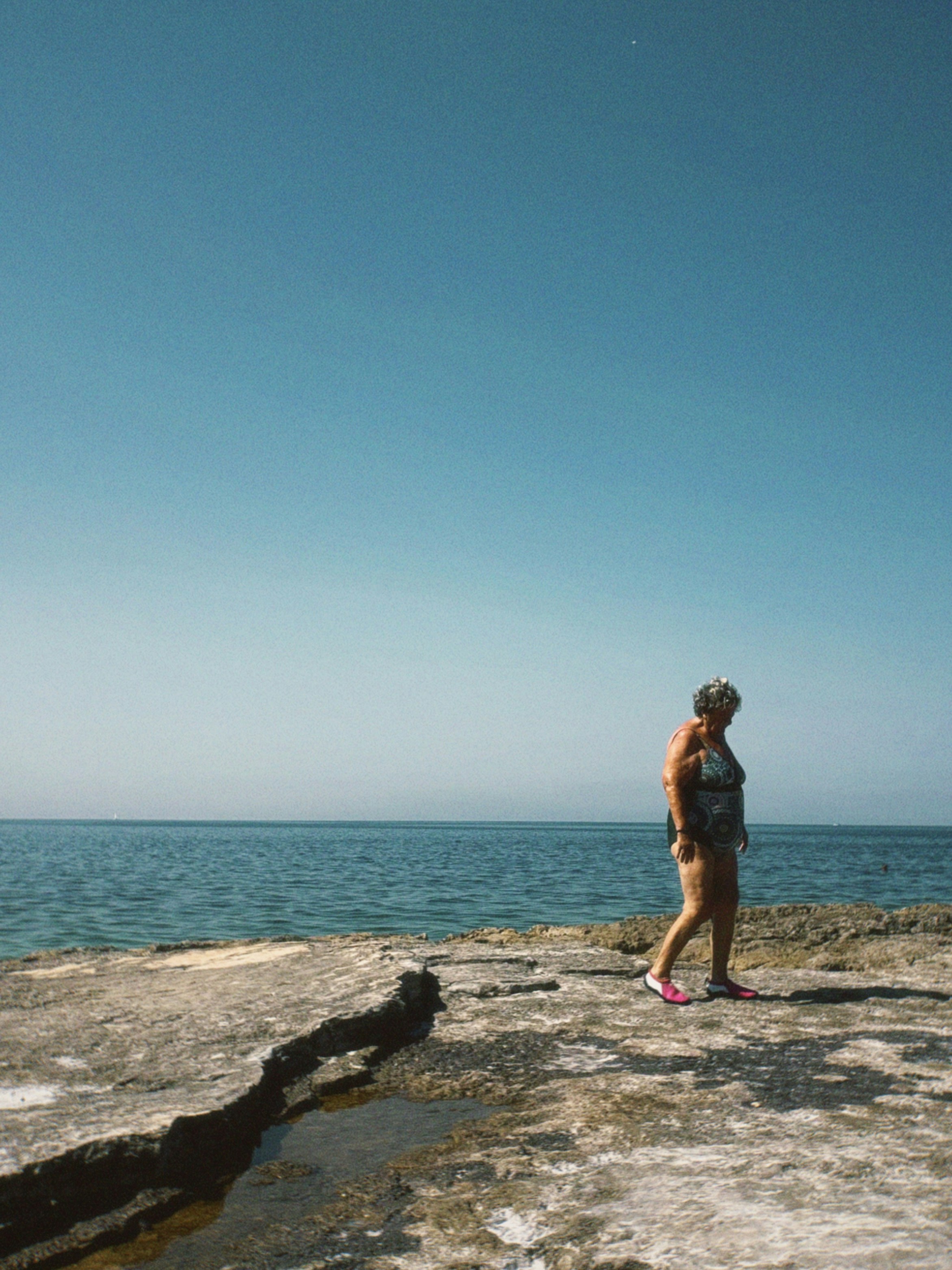 A woman walks along a rocky shore by the ocean.
