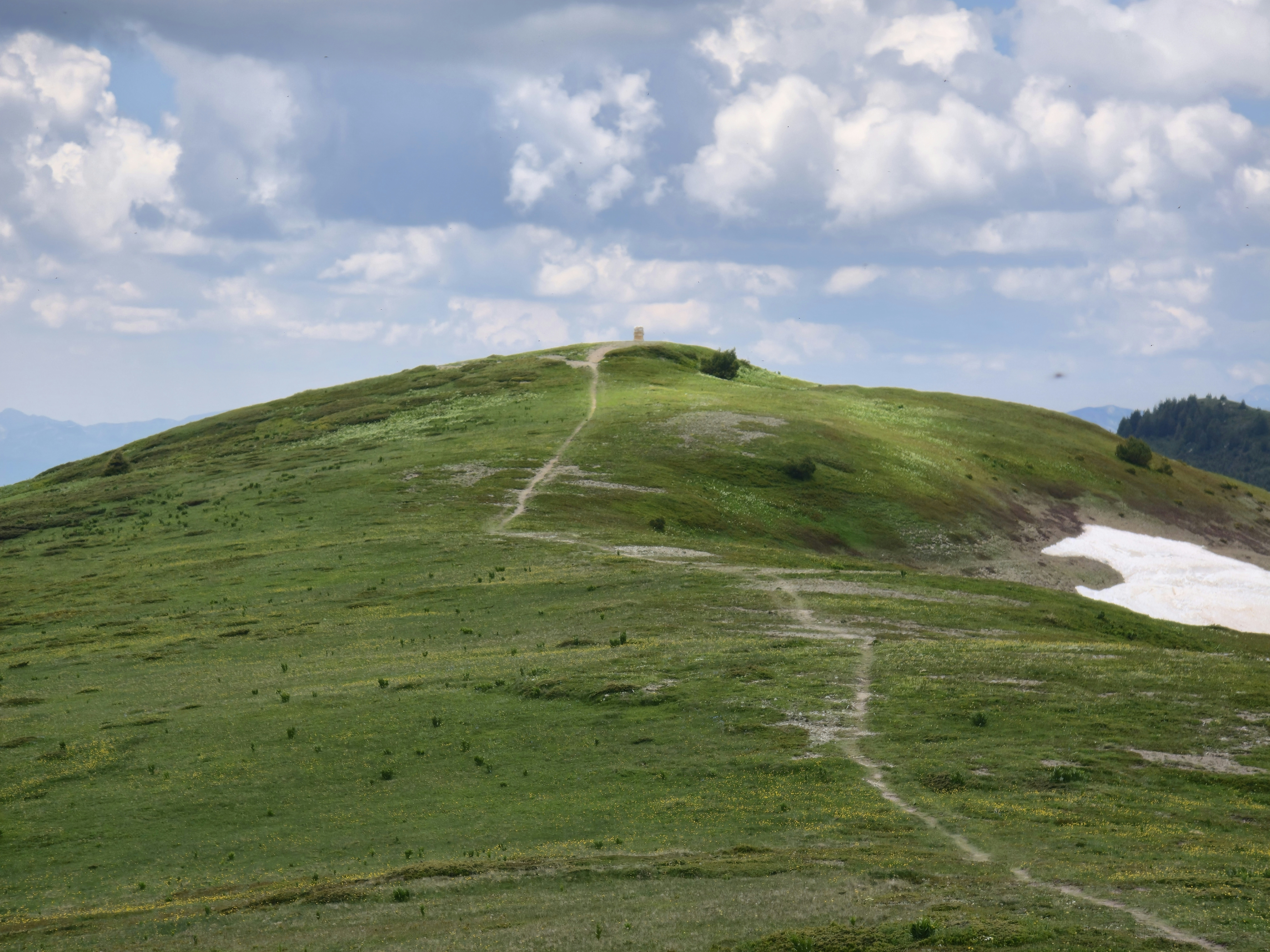 Grassy mountain peak with winding path and cloudy sky.