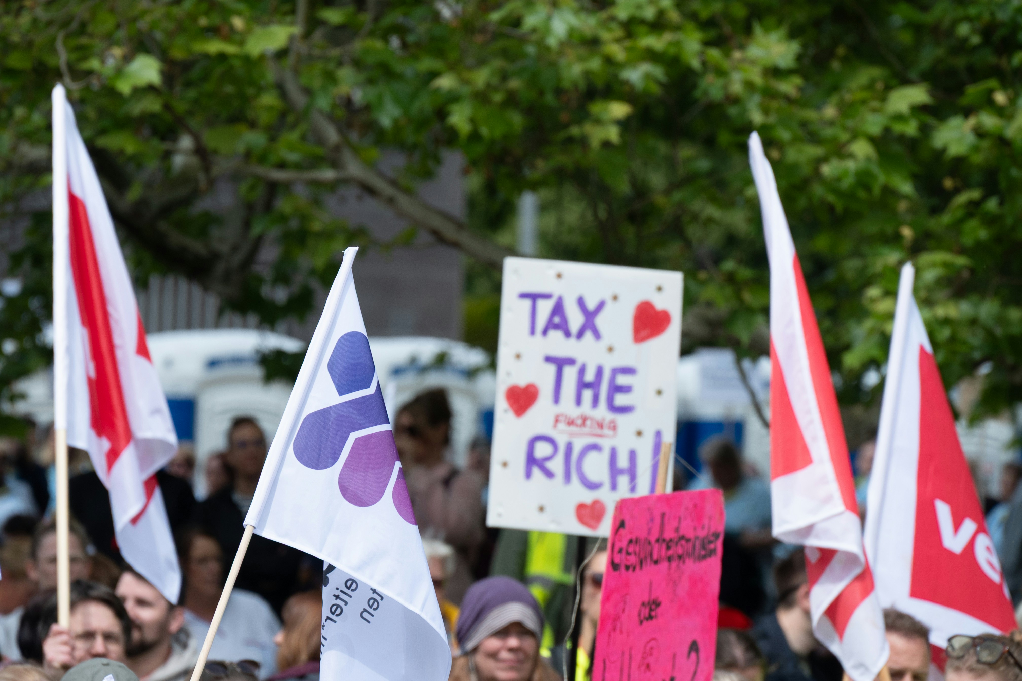 Menschen, die mit Flaggen und einem "Besteuert die Reichen"-Schild protestieren.