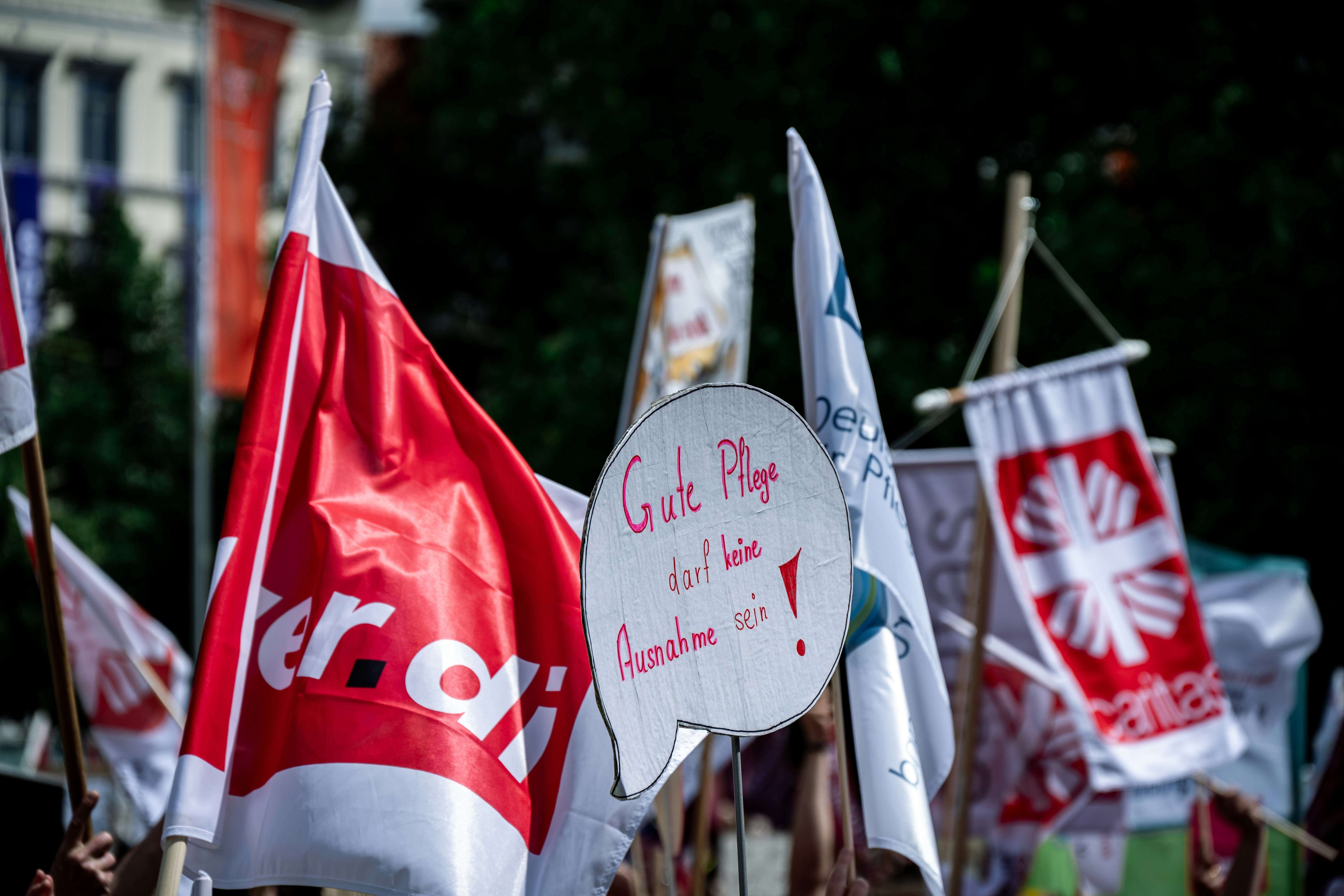 Rote ver.di- und Caritas-Flaggen mit Protestschild bei der Demonstration.