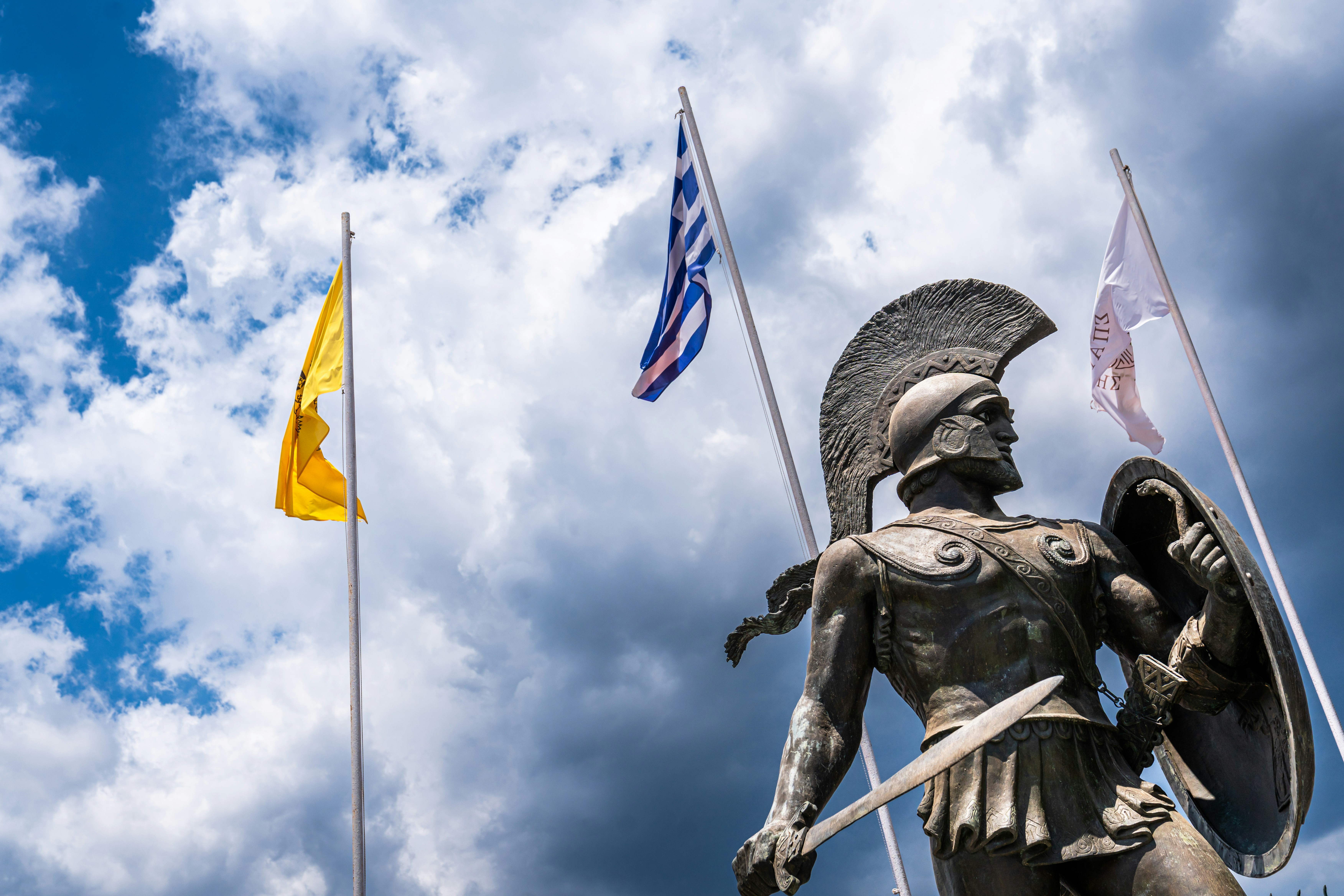 Spartan warrior statue and flags against a cloudy sky