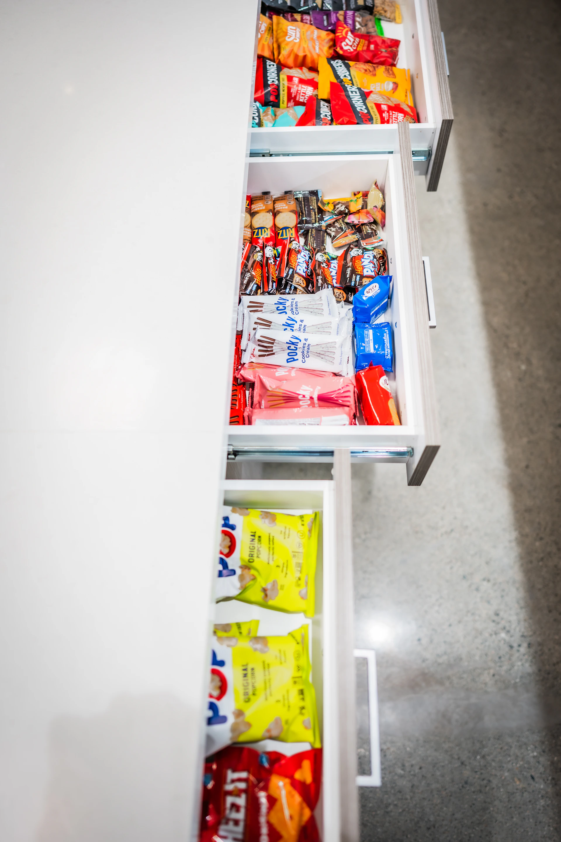 Three open drawers filled with an assortment of packaged snacks