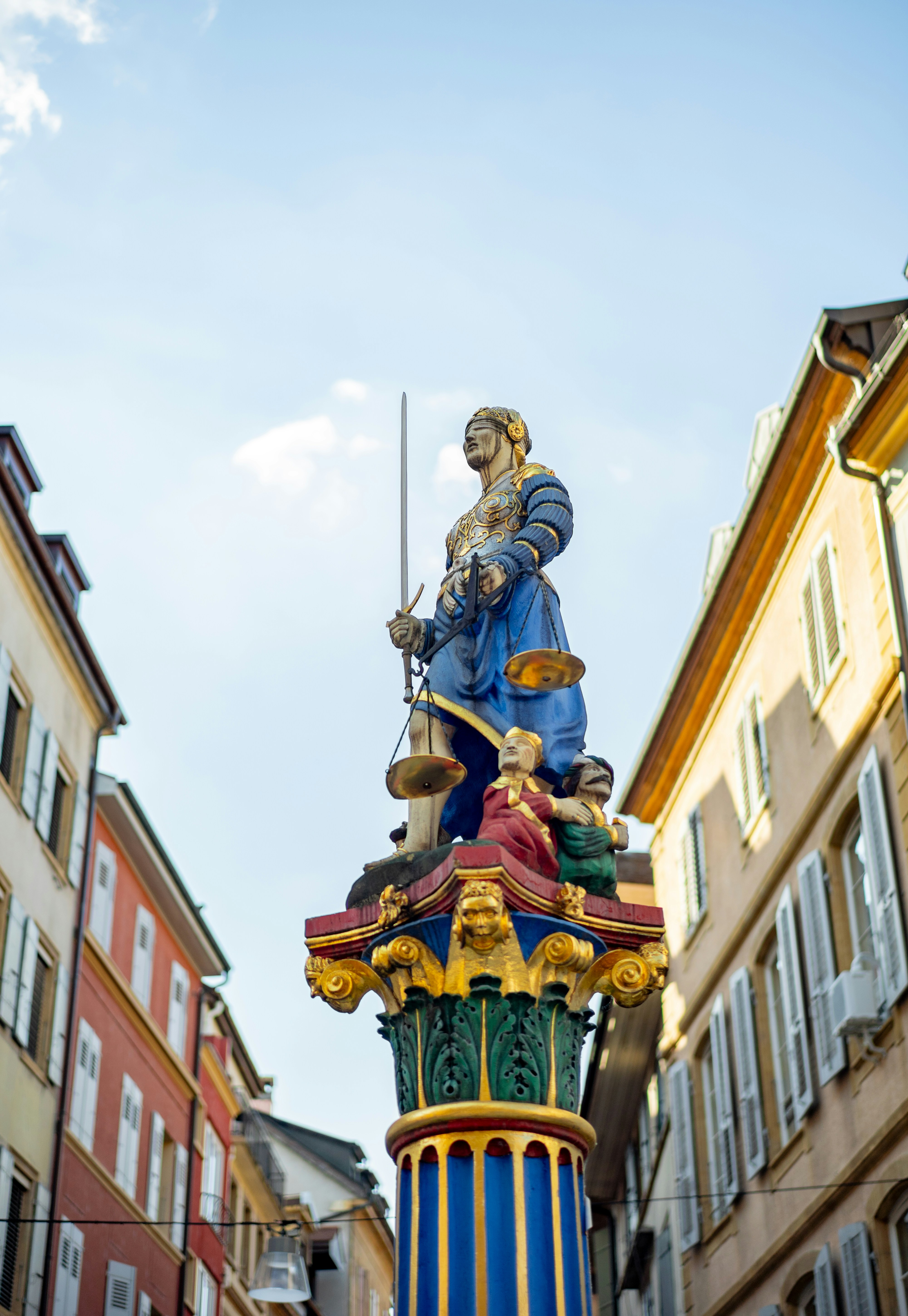 Lady justice statue on colorful fountain in european street.
