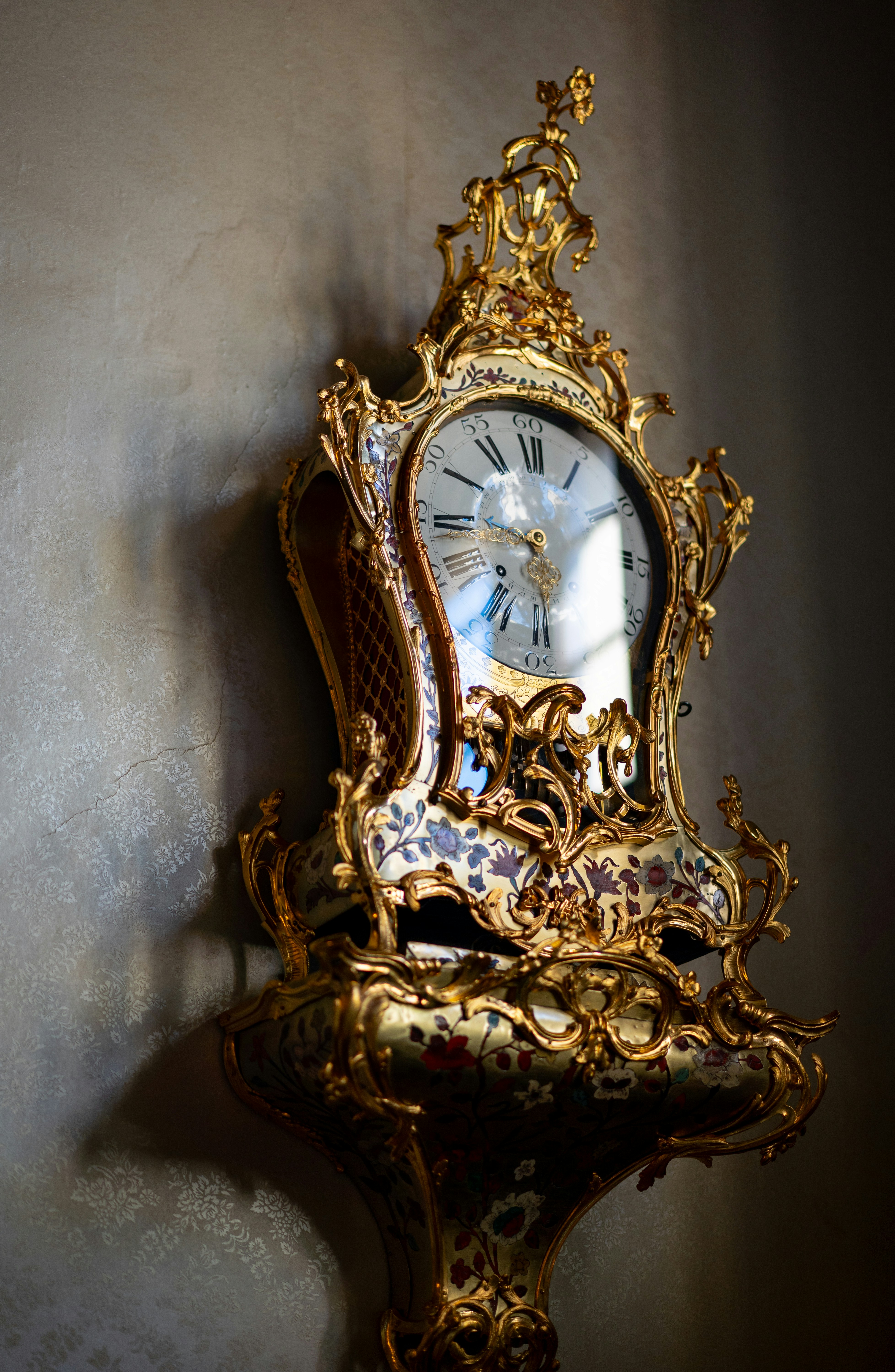 Beautiful ornate golden antique clock against a textured wall.