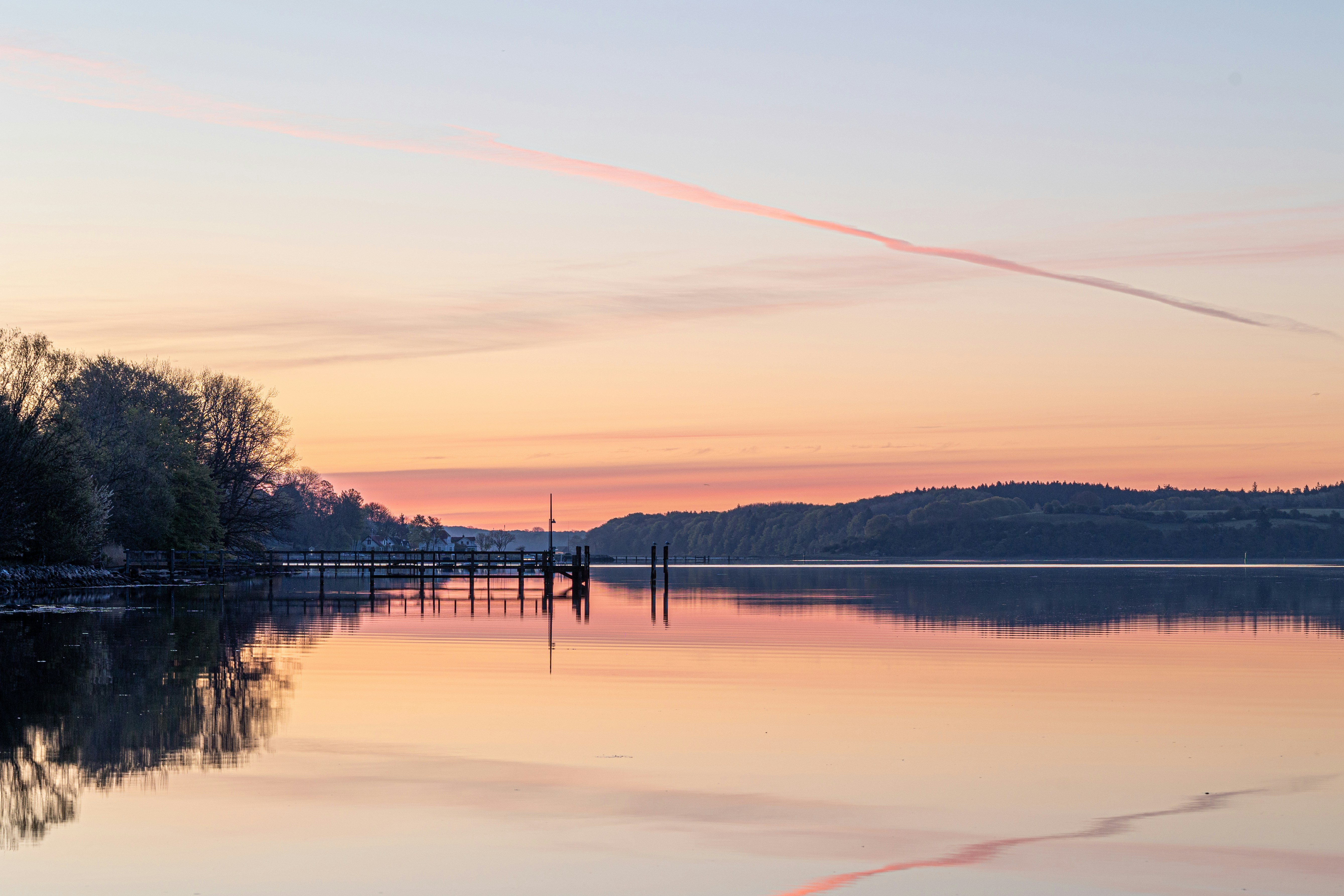 Serene lake reflects colorful sunrise sky with distant hills.