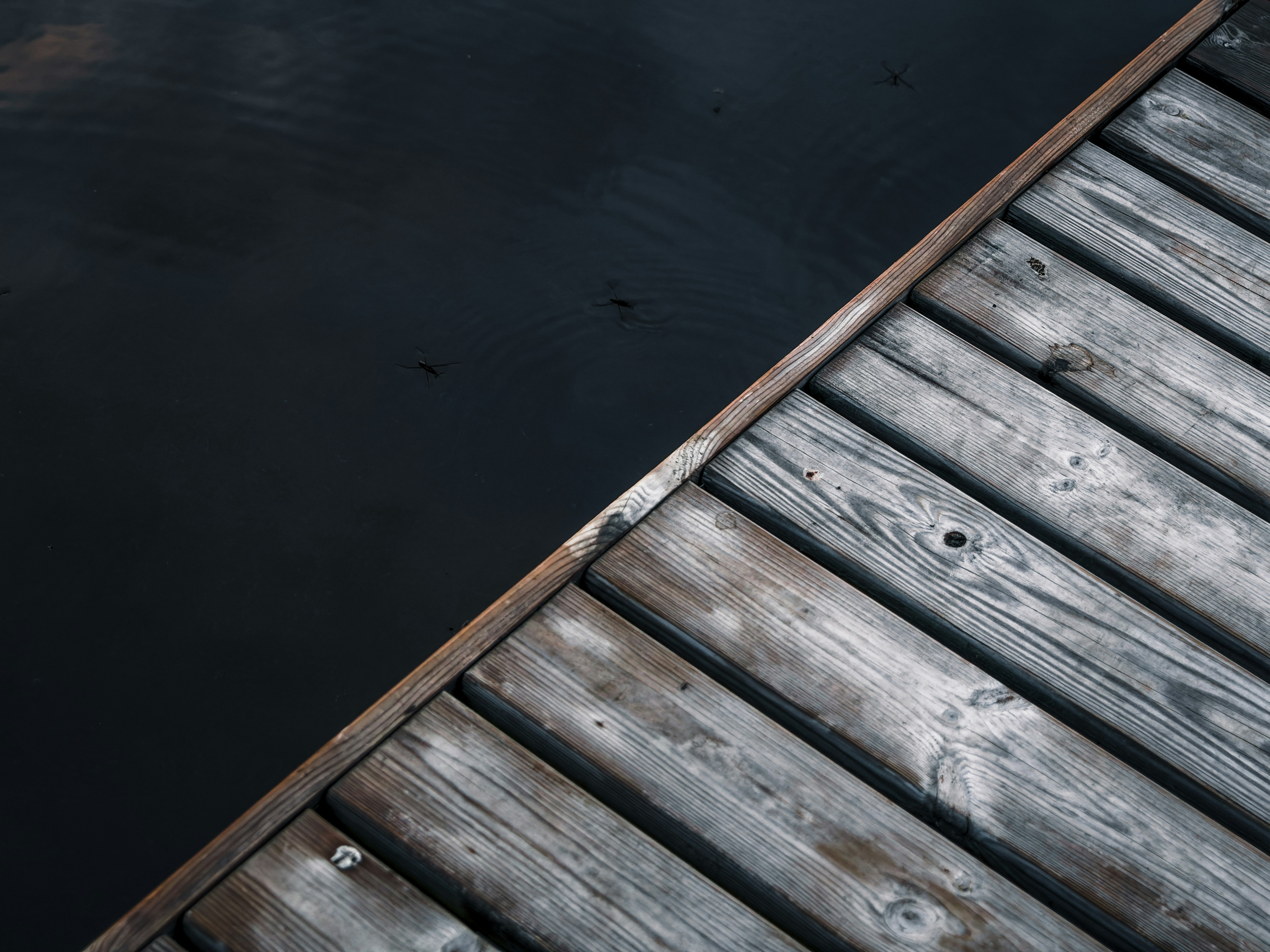 A weathered wooden dock meets dark, calm water.