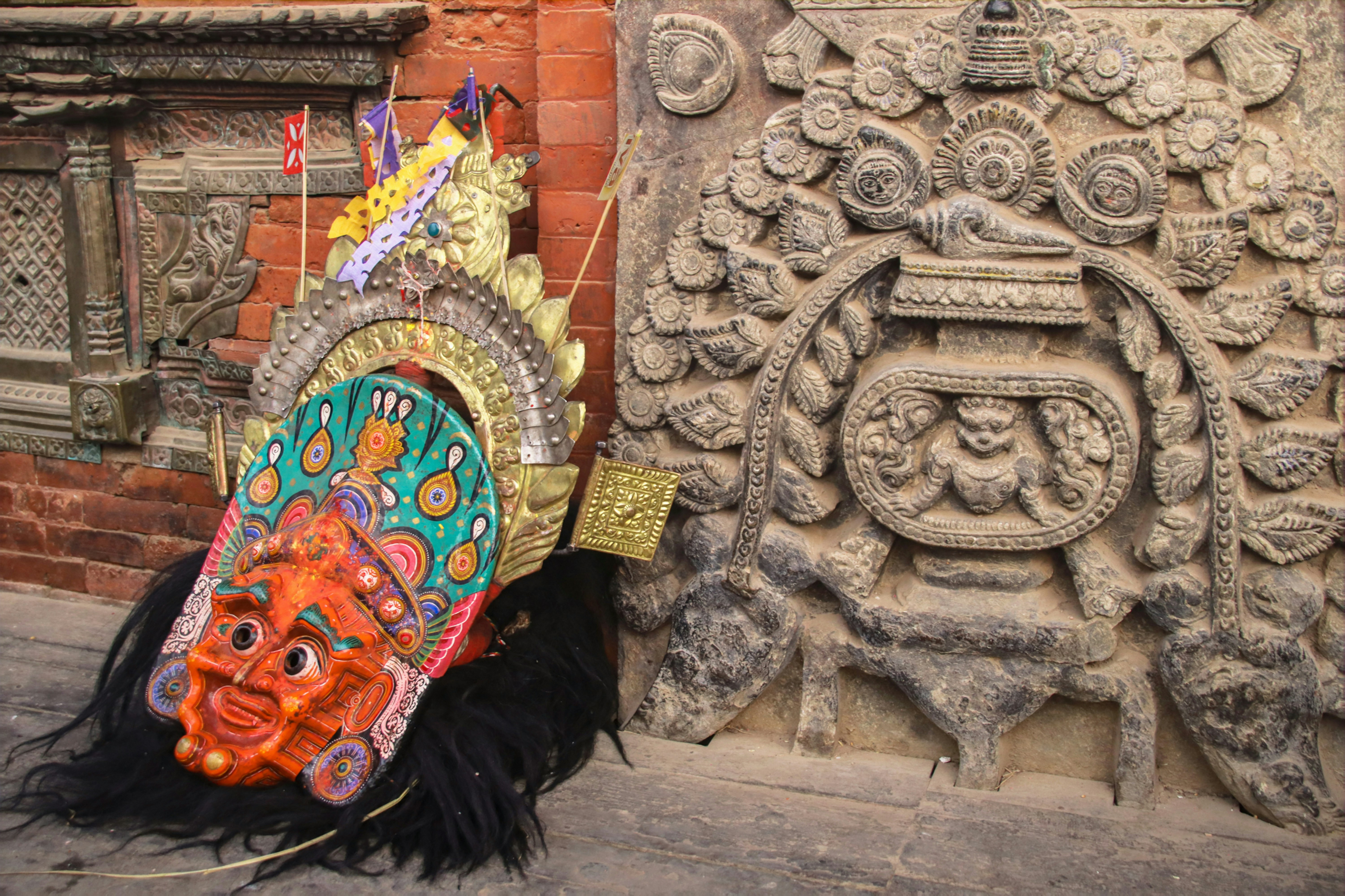 Topeng tradisional berwarna-warni bertumpu pada ukiran batu kuno.