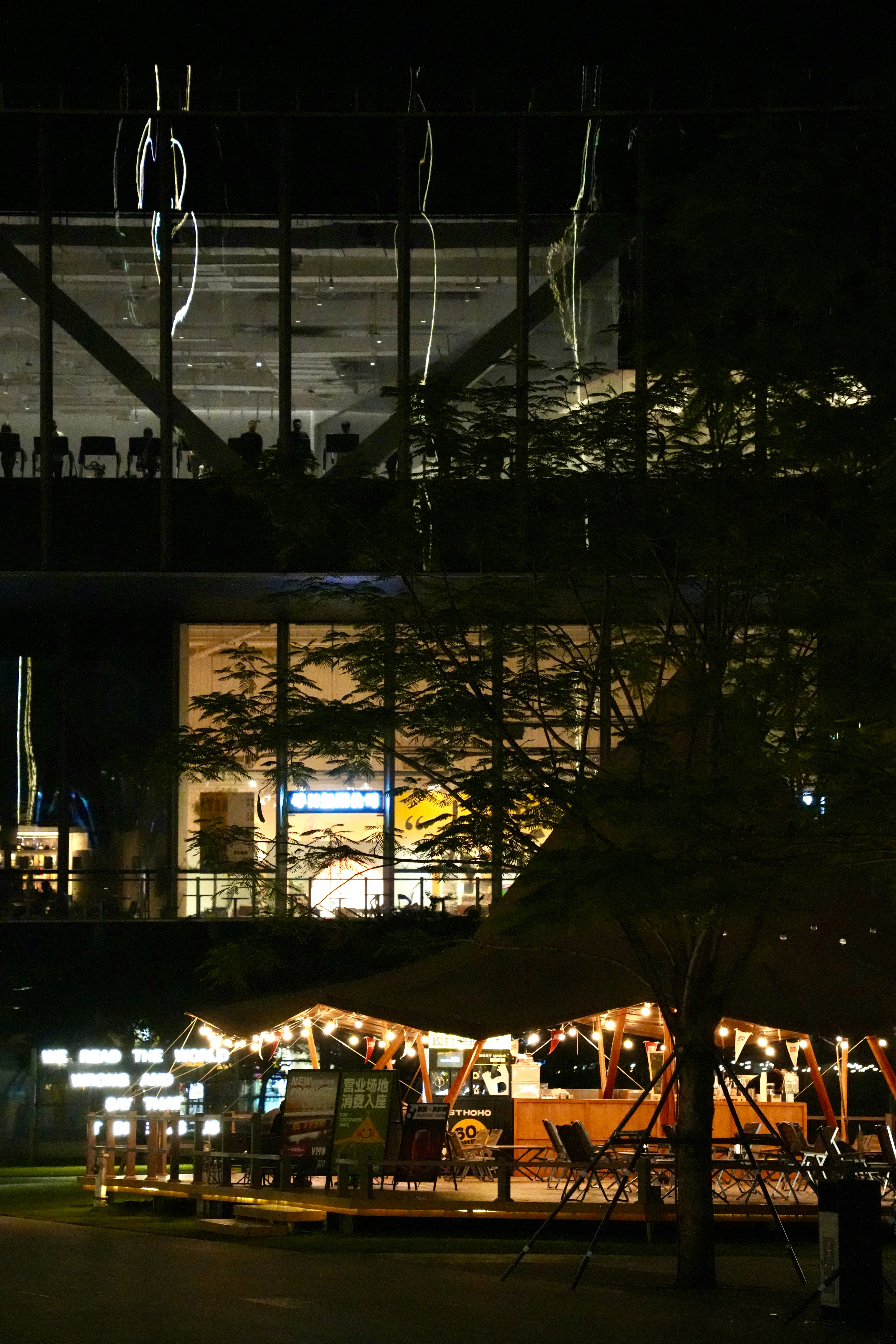A vibrant outdoor cafe at night below a modern building