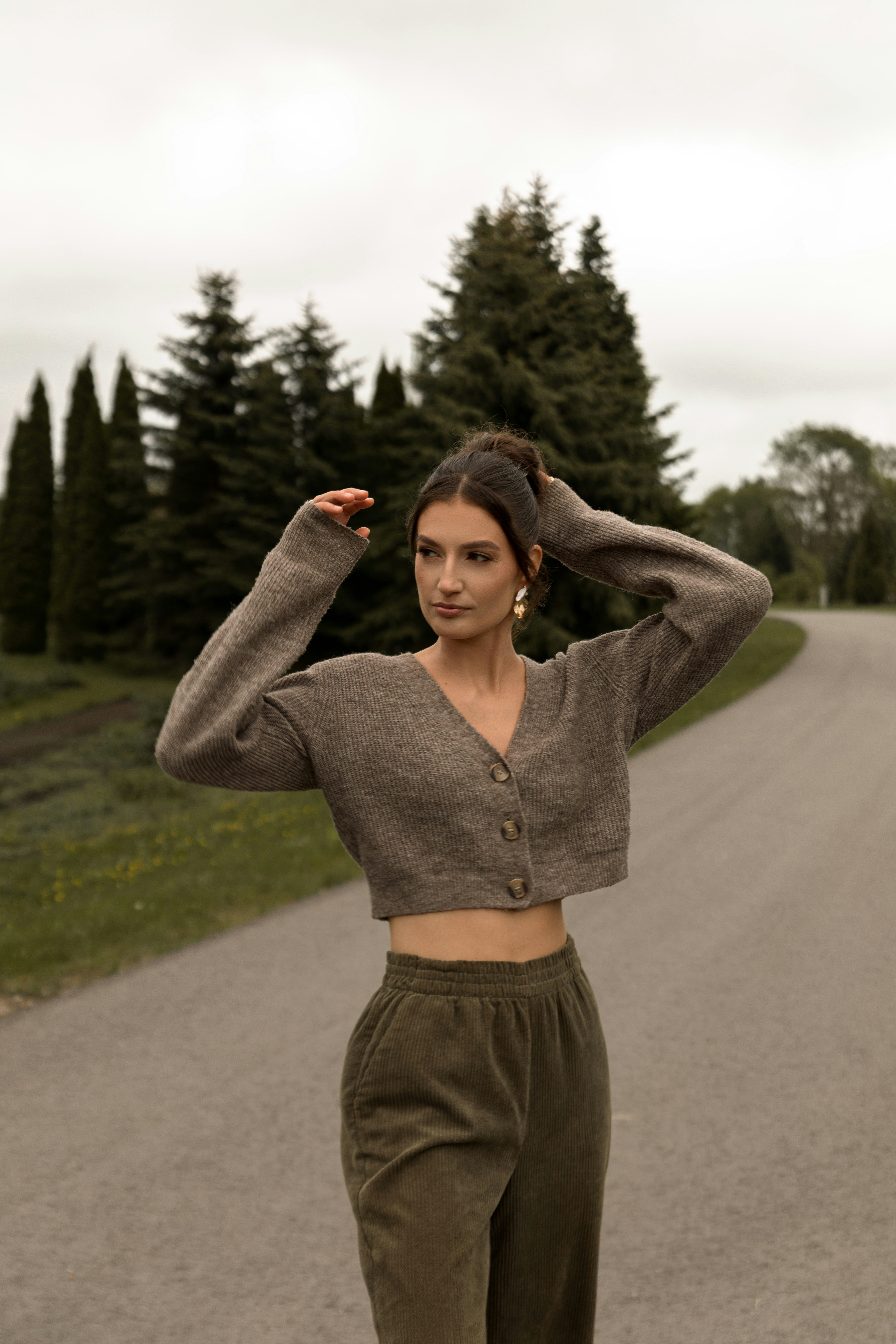 Jovem posando em uma estrada com árvores perenes.
