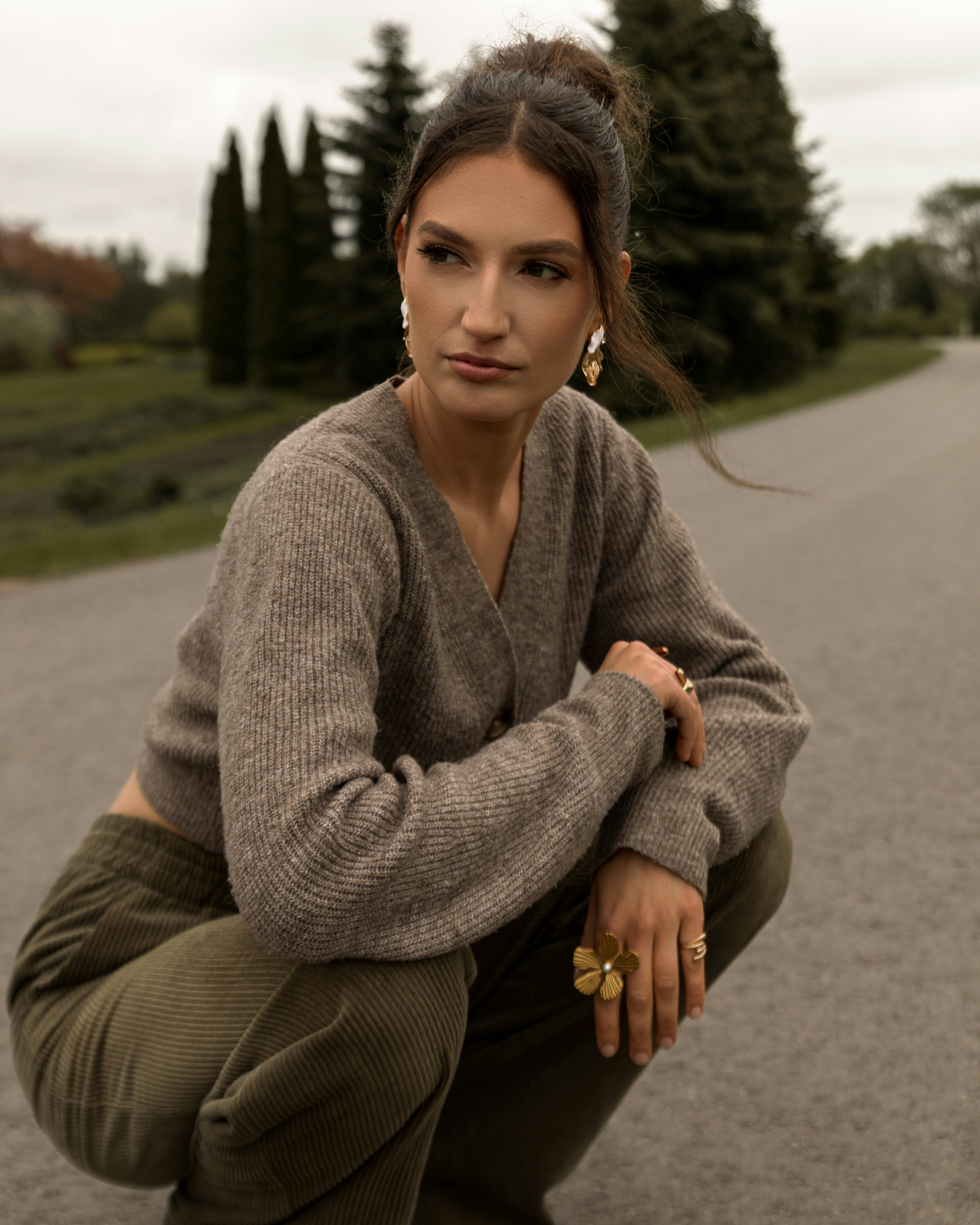 Mulher elegante de cardigã marrom e calça verde ao ar livre.