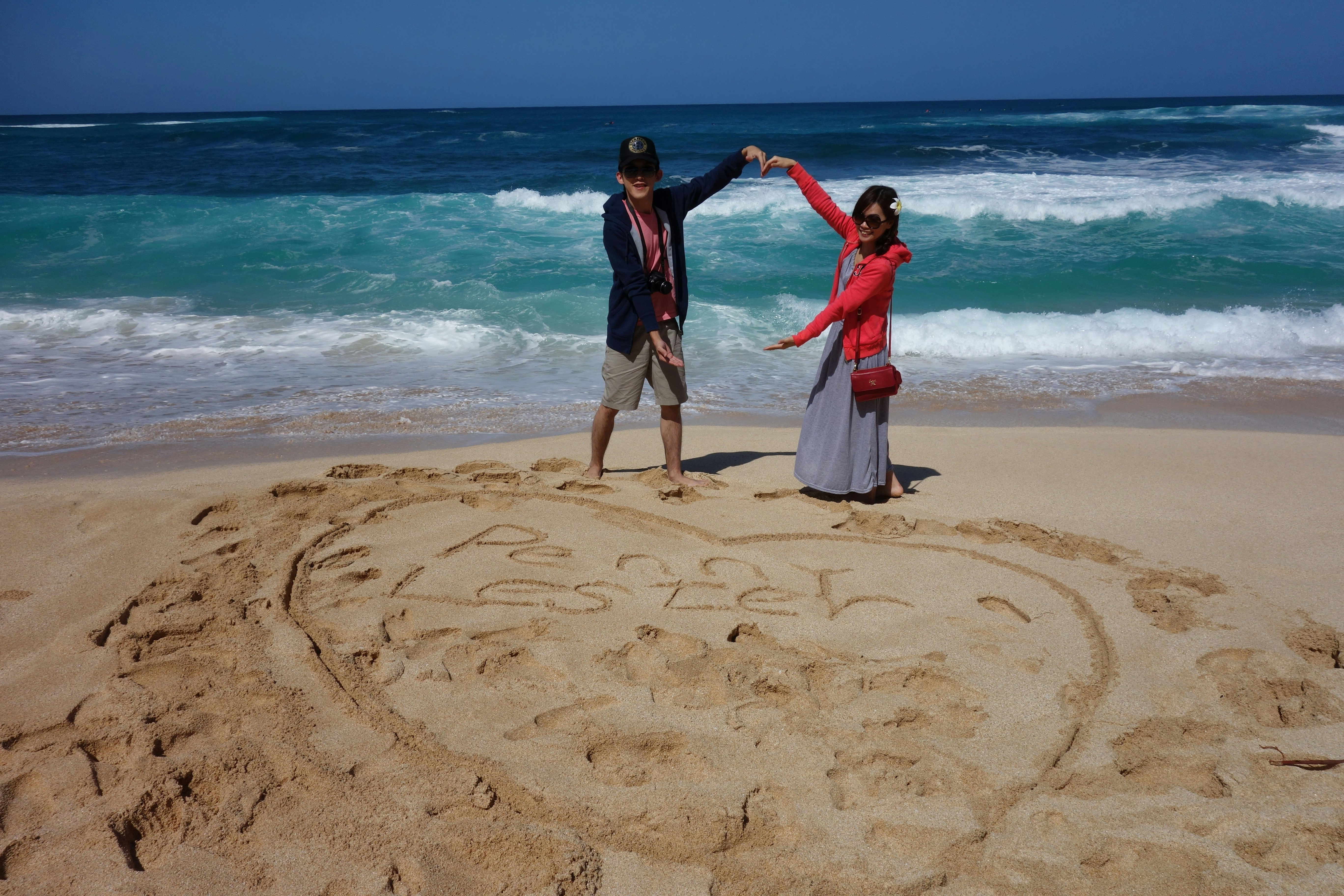 Couple posing on a sandy beach with heart in sand.