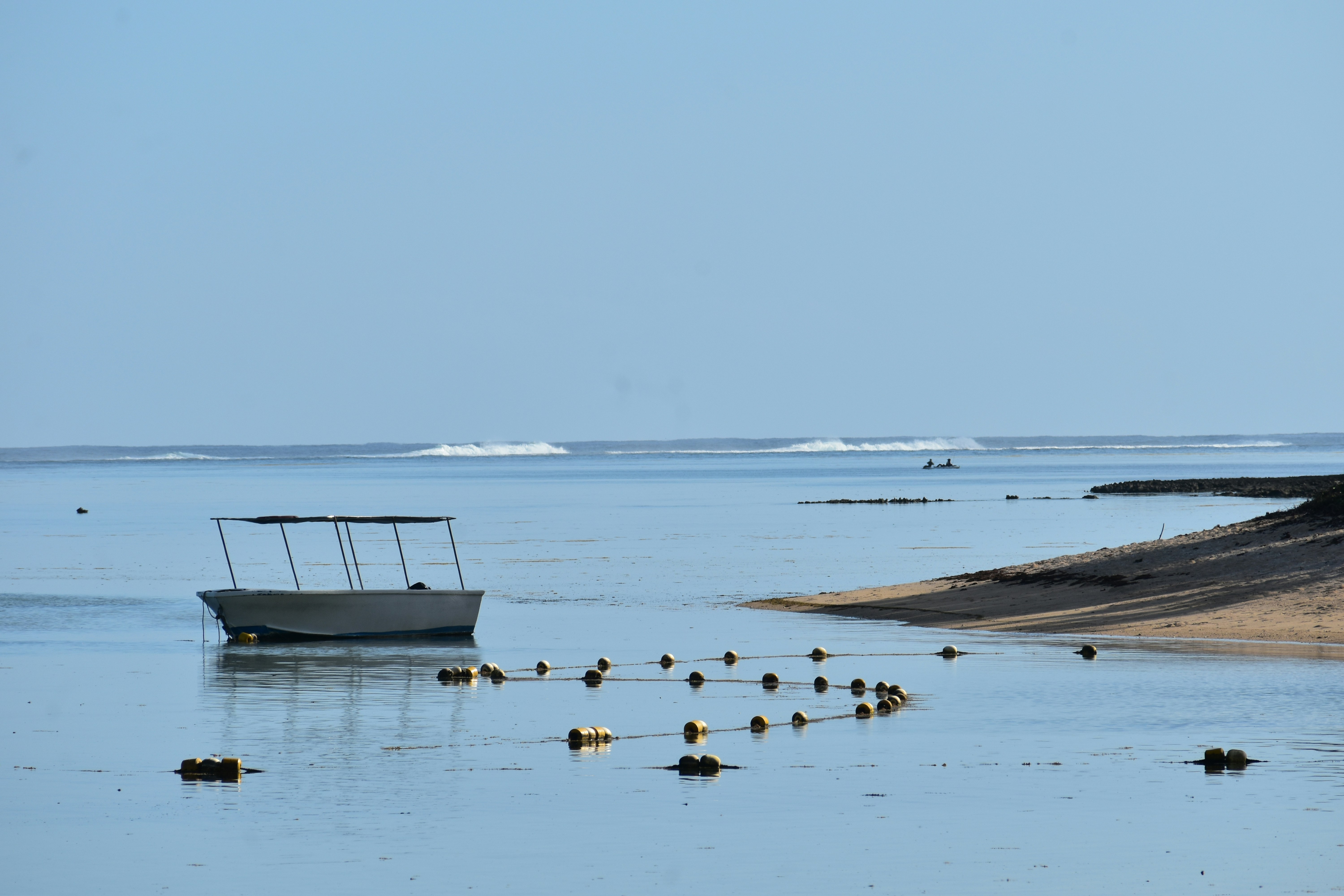 Small boat anchored near shore with buoys in calm ocean.