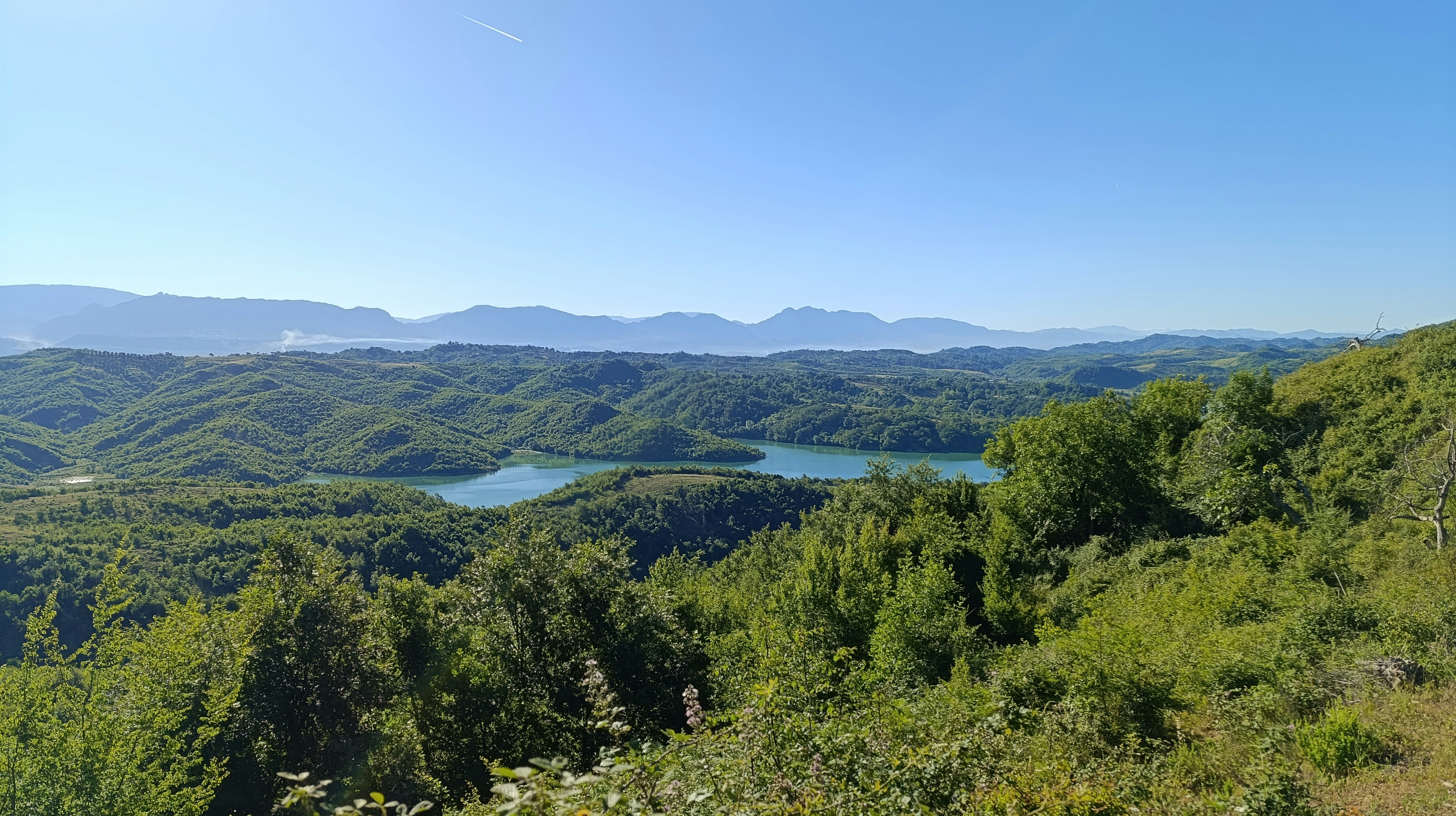 Panoramic view of green hills, a lake, and distant mountains.