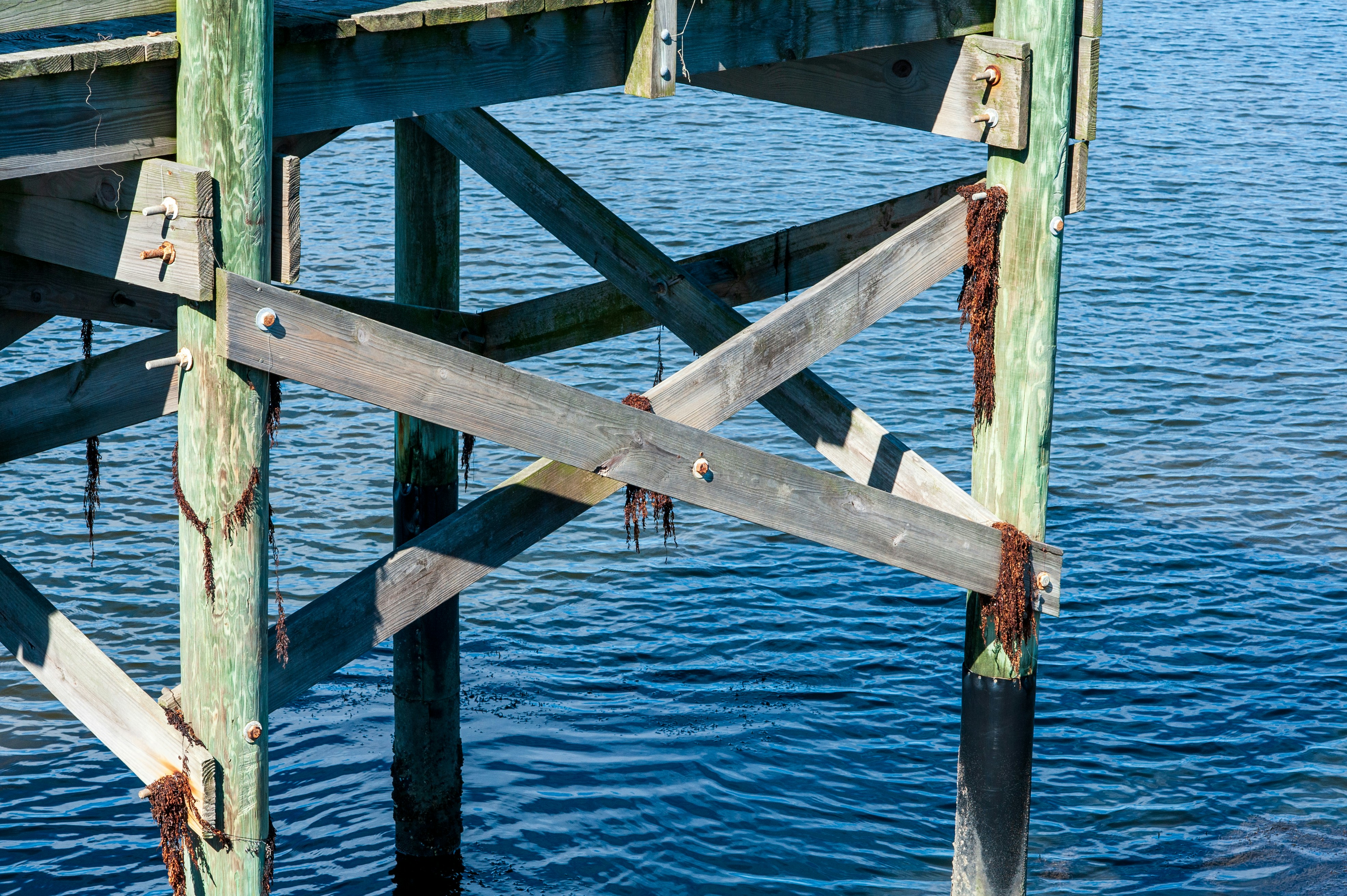 Wooden pier supports with metal crossbeams over blue water.