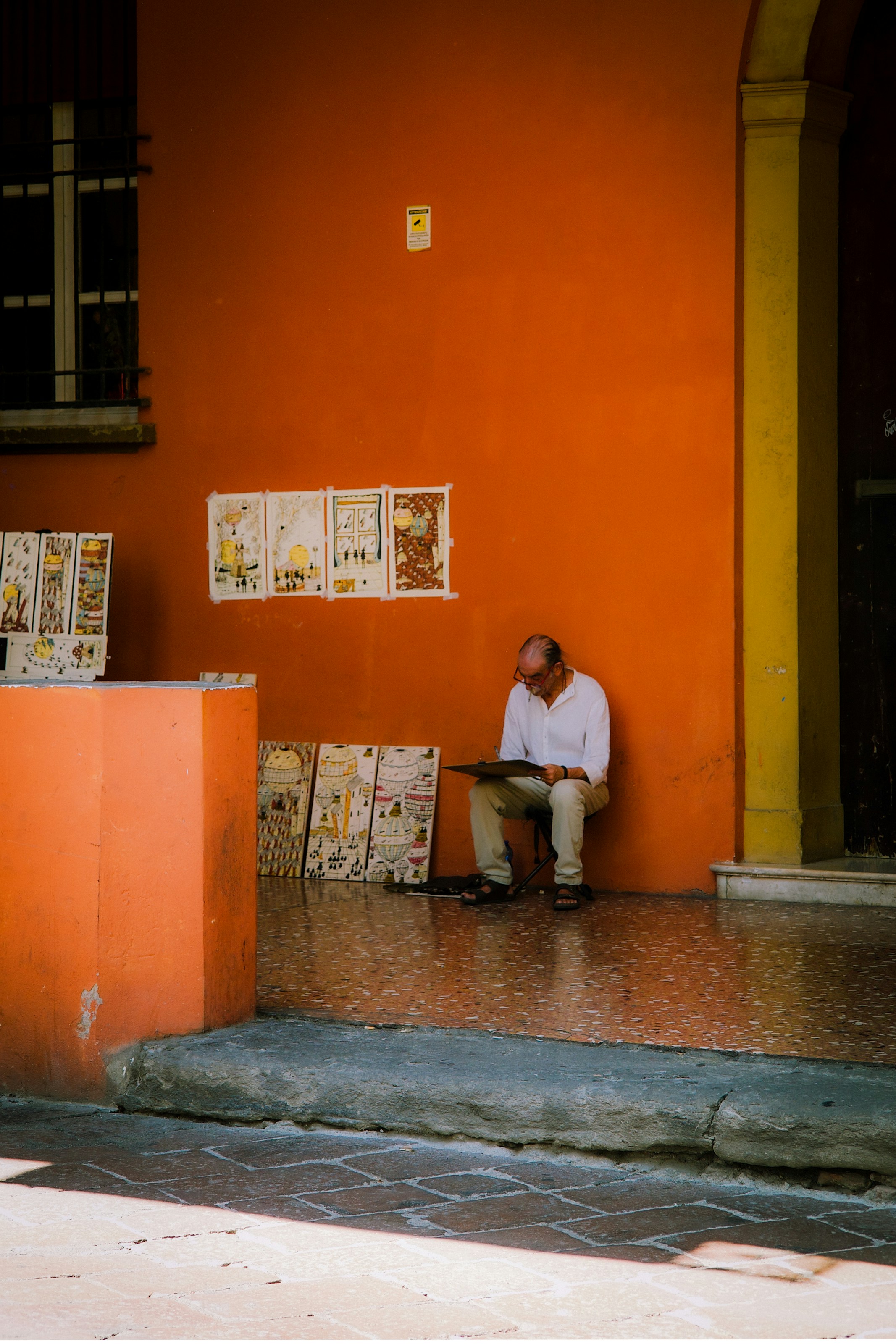 Man sits against orange wall surrounded by displayed artwork