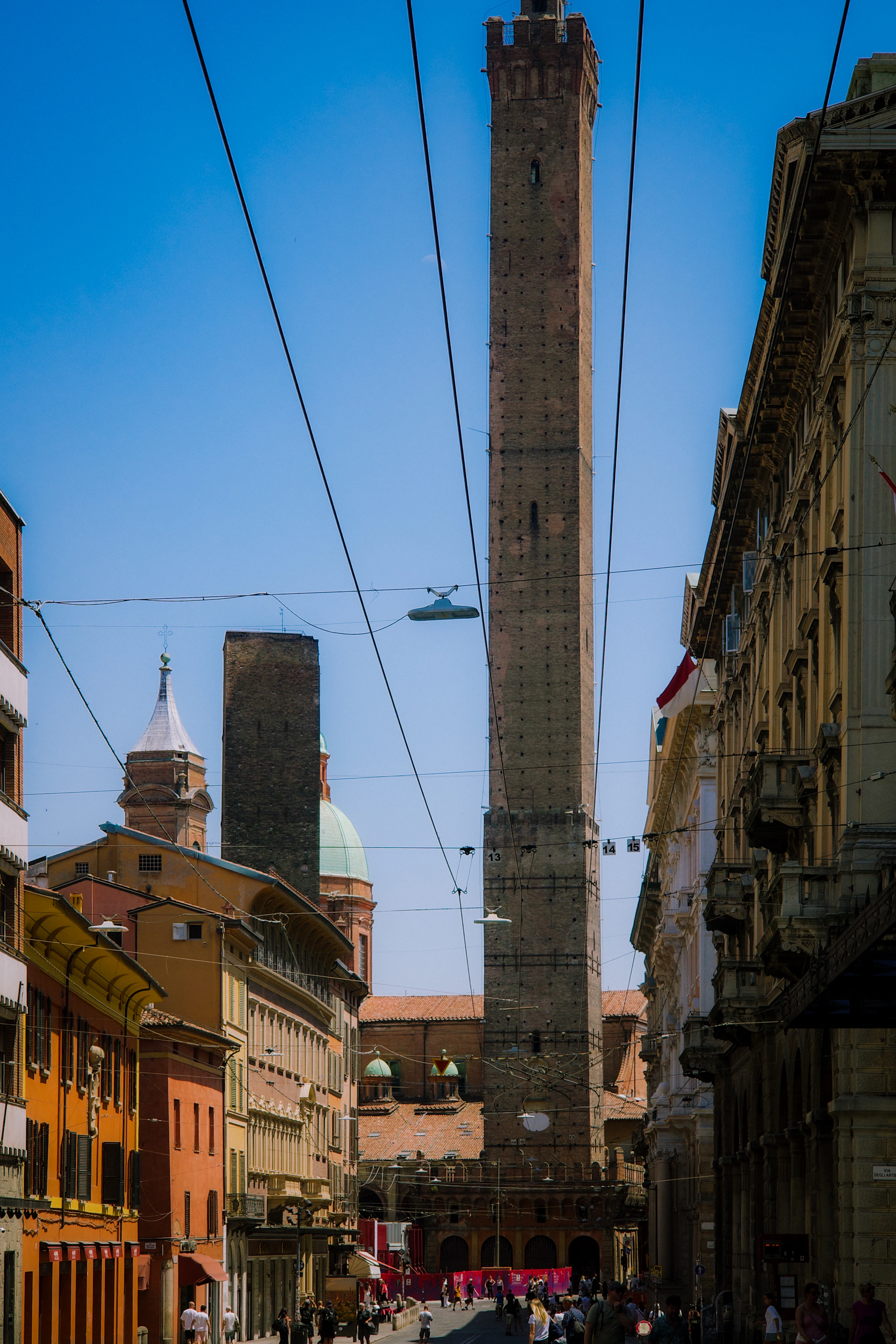 Bologna's leaning Two Towers, Asinelli and Garisenda, rising above a street of ochre buildings and overhead tram wires