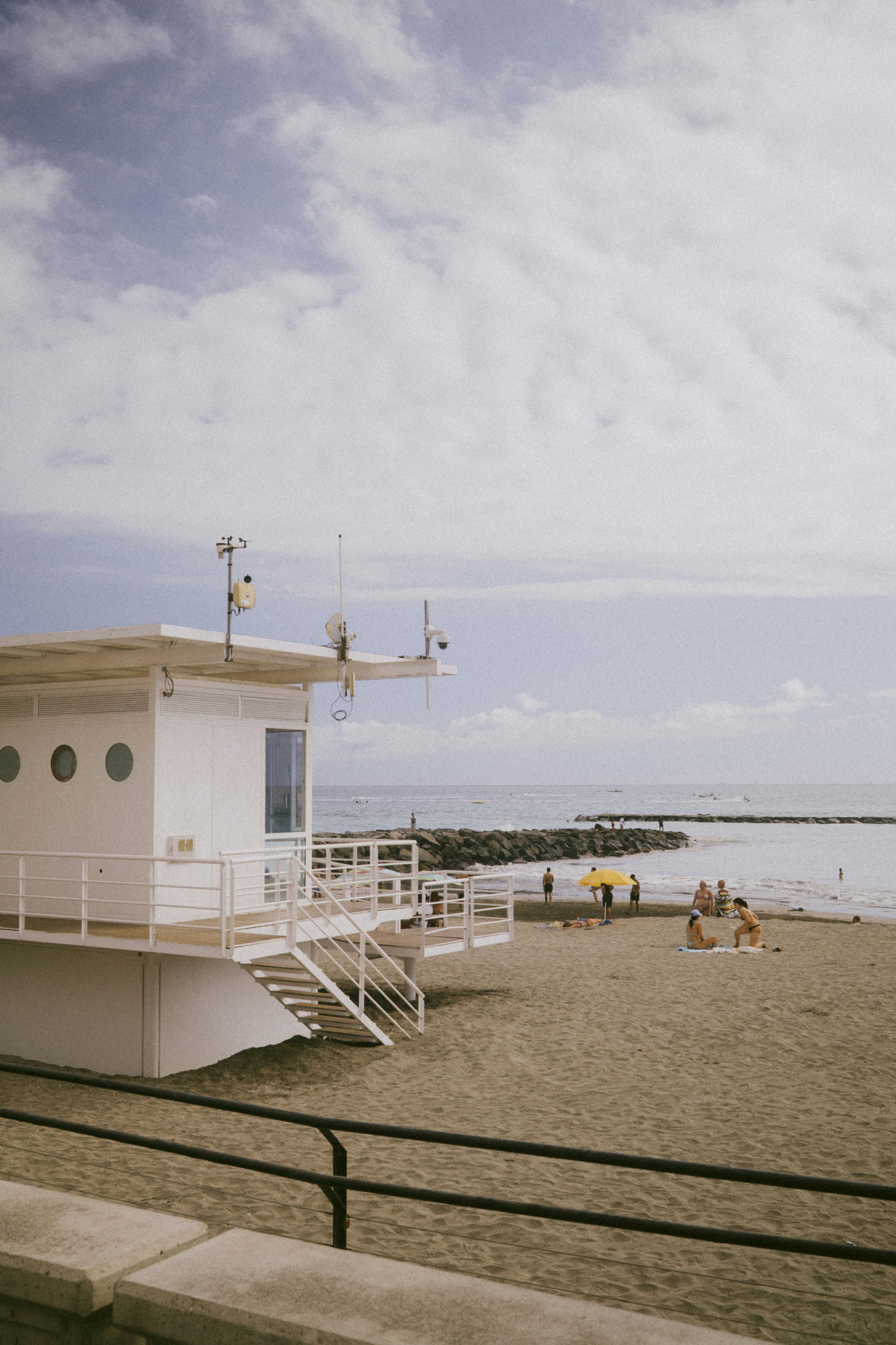 White beach building overlooks sandy shore with people and ocean.
