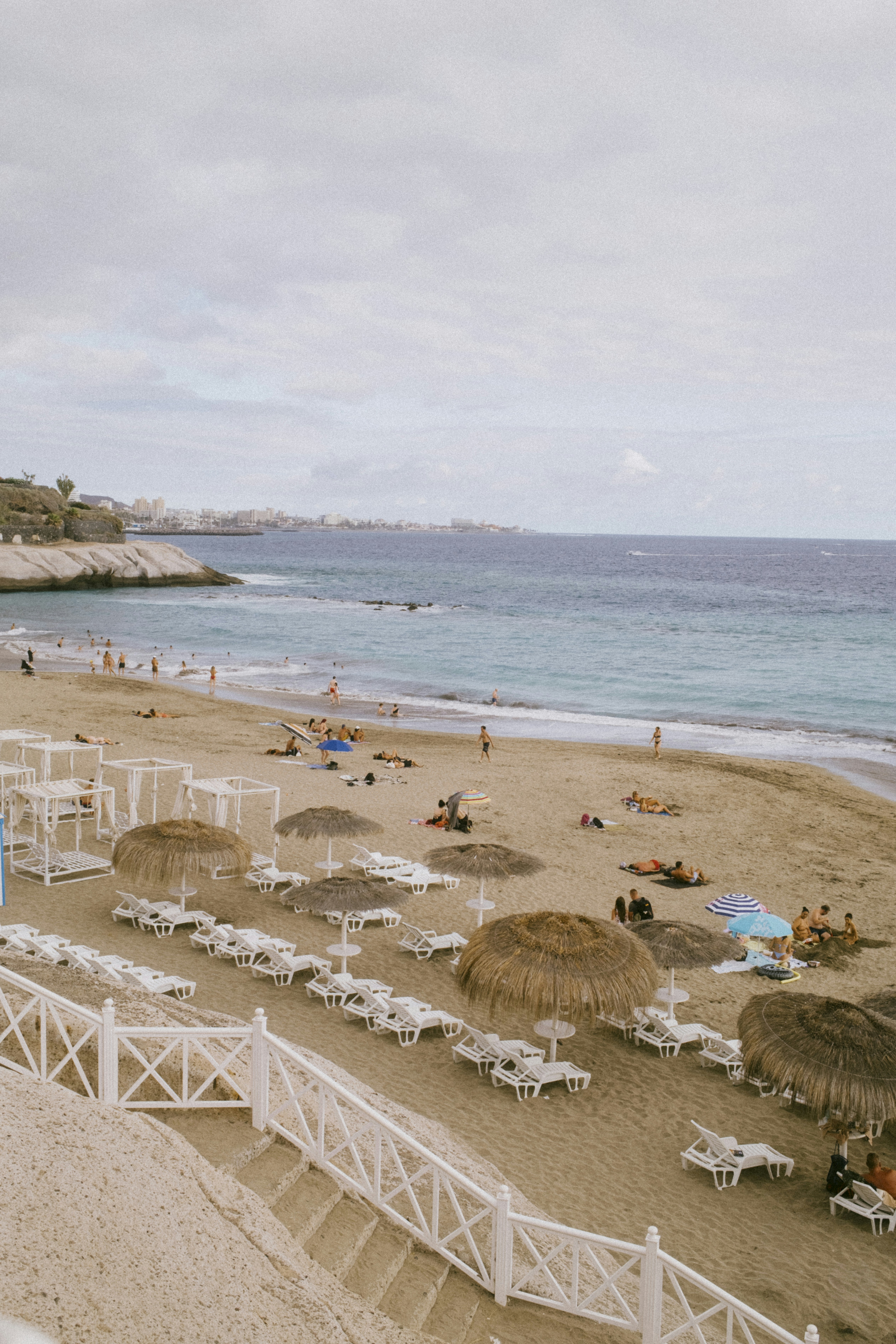 Sandy beach with straw umbrellas, lounge chairs, and blue sea.