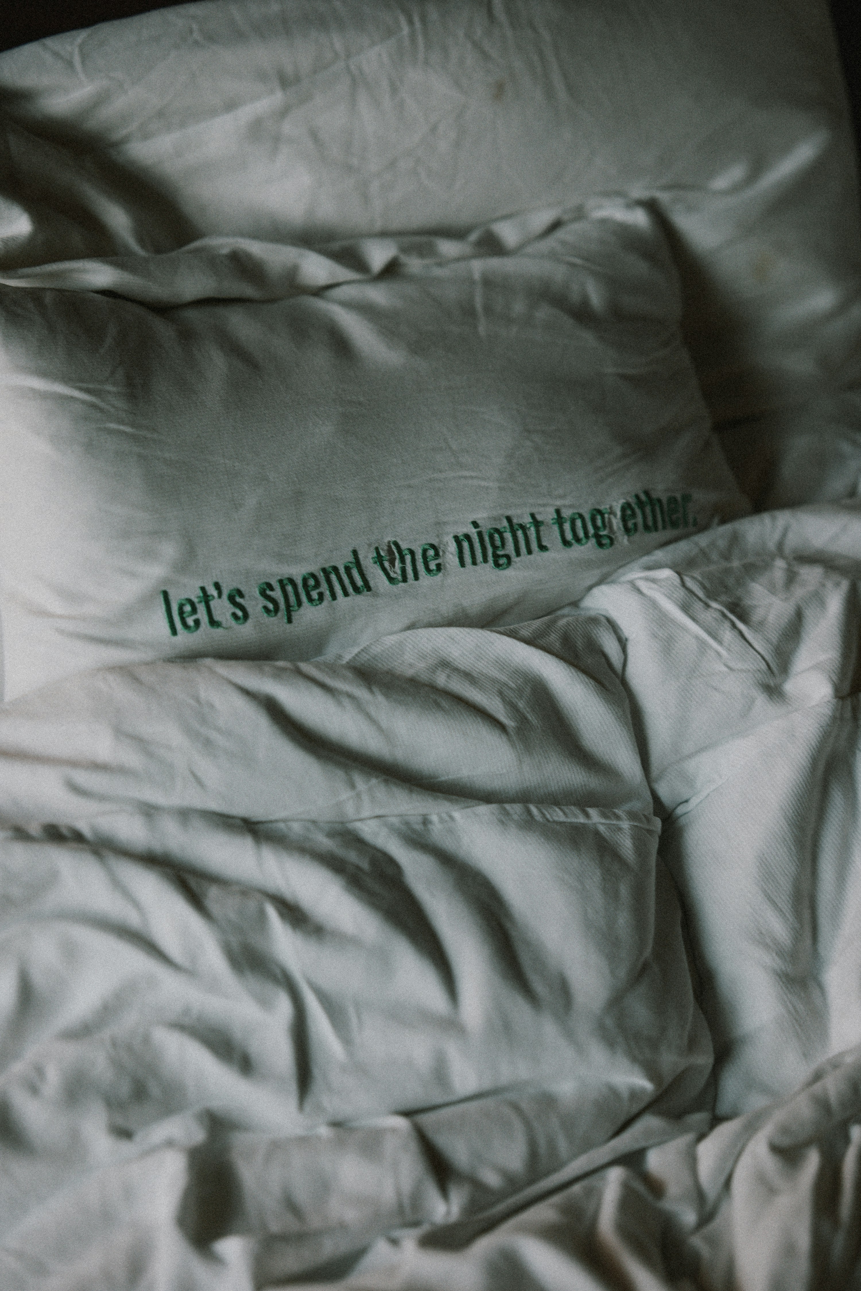 Rumpled white bed with a pillow featuring romantic text