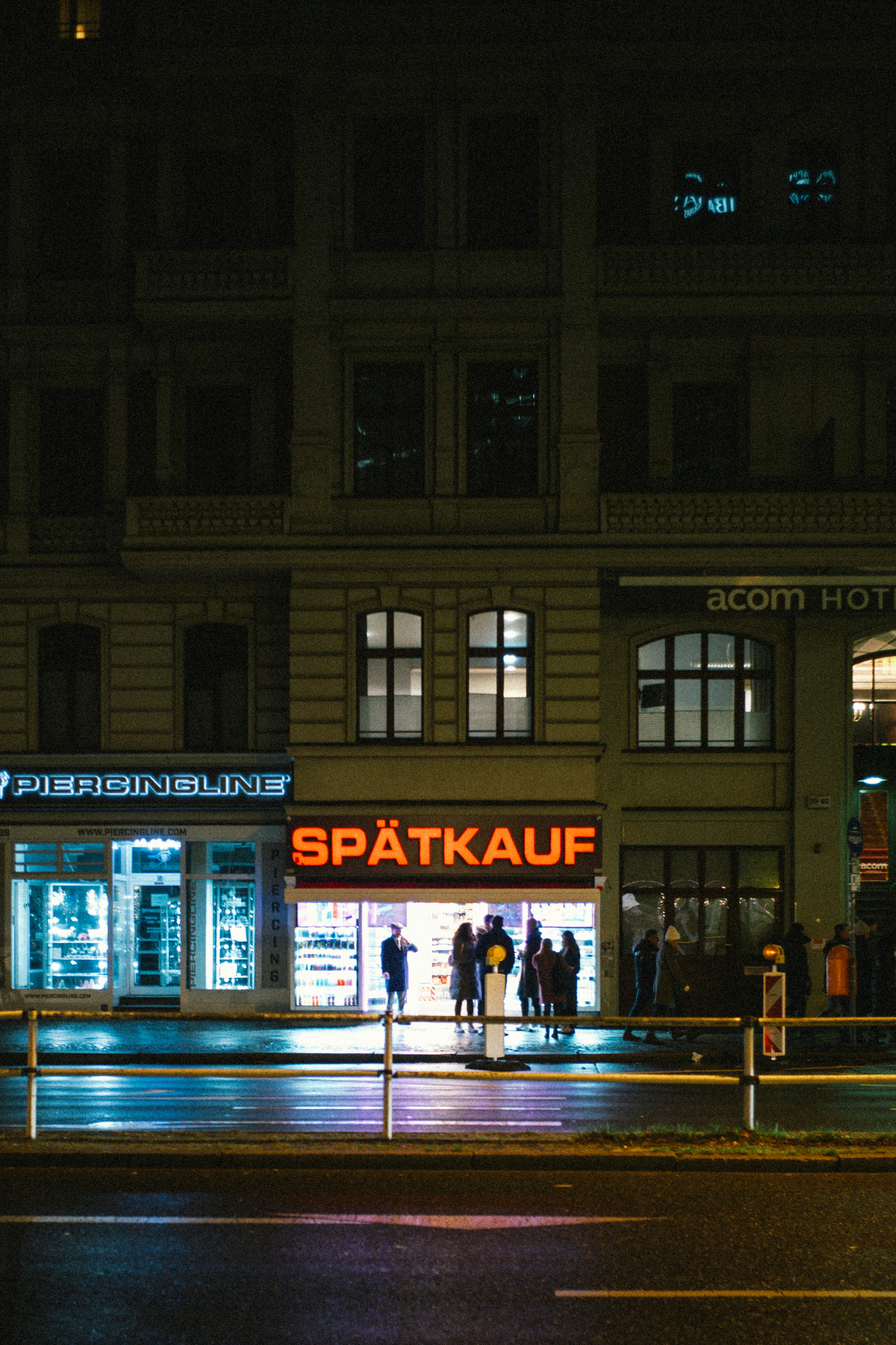 People gather outside a brightly lit spätkauf store at night