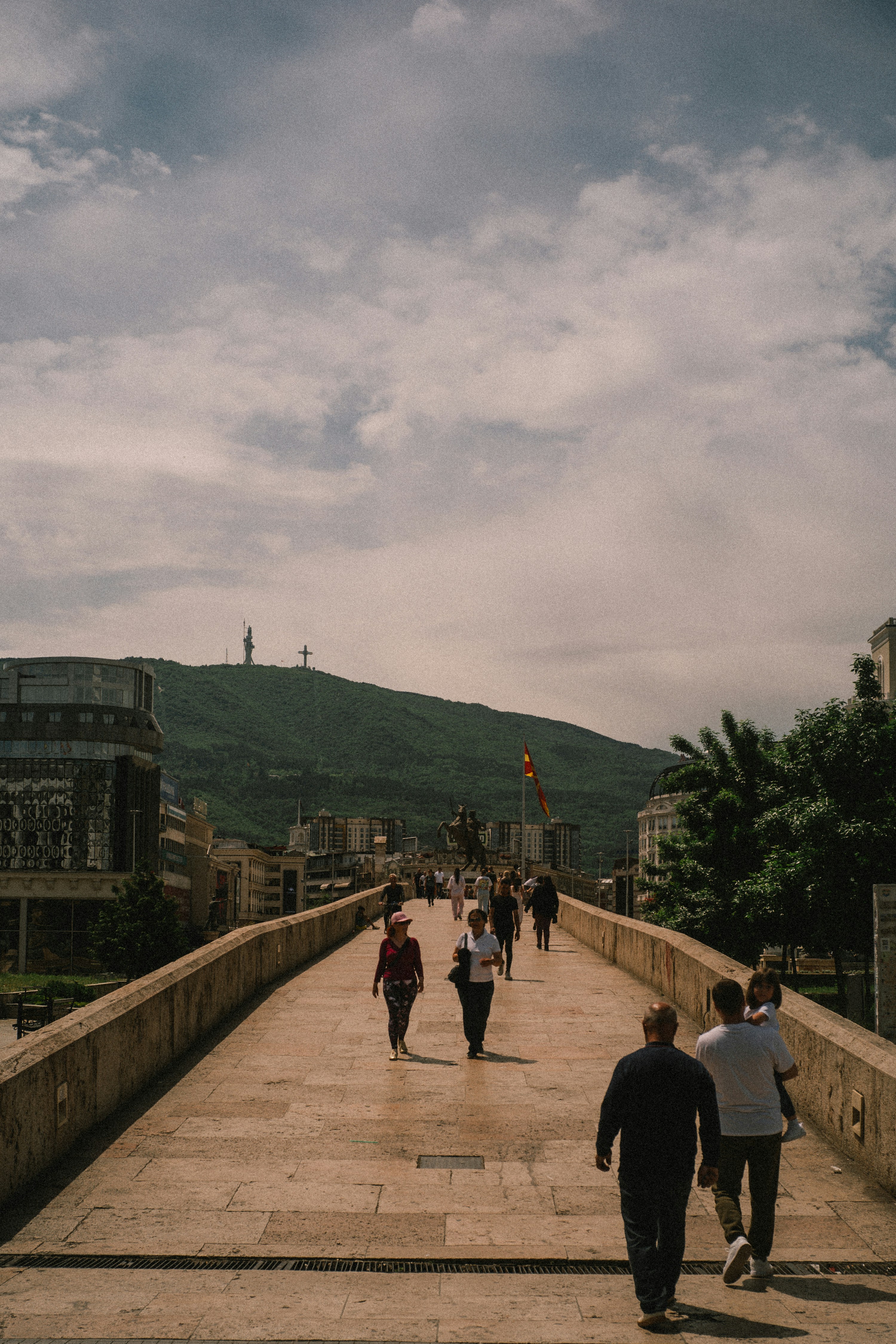 People walk on a stone bridge towards a distant mountain