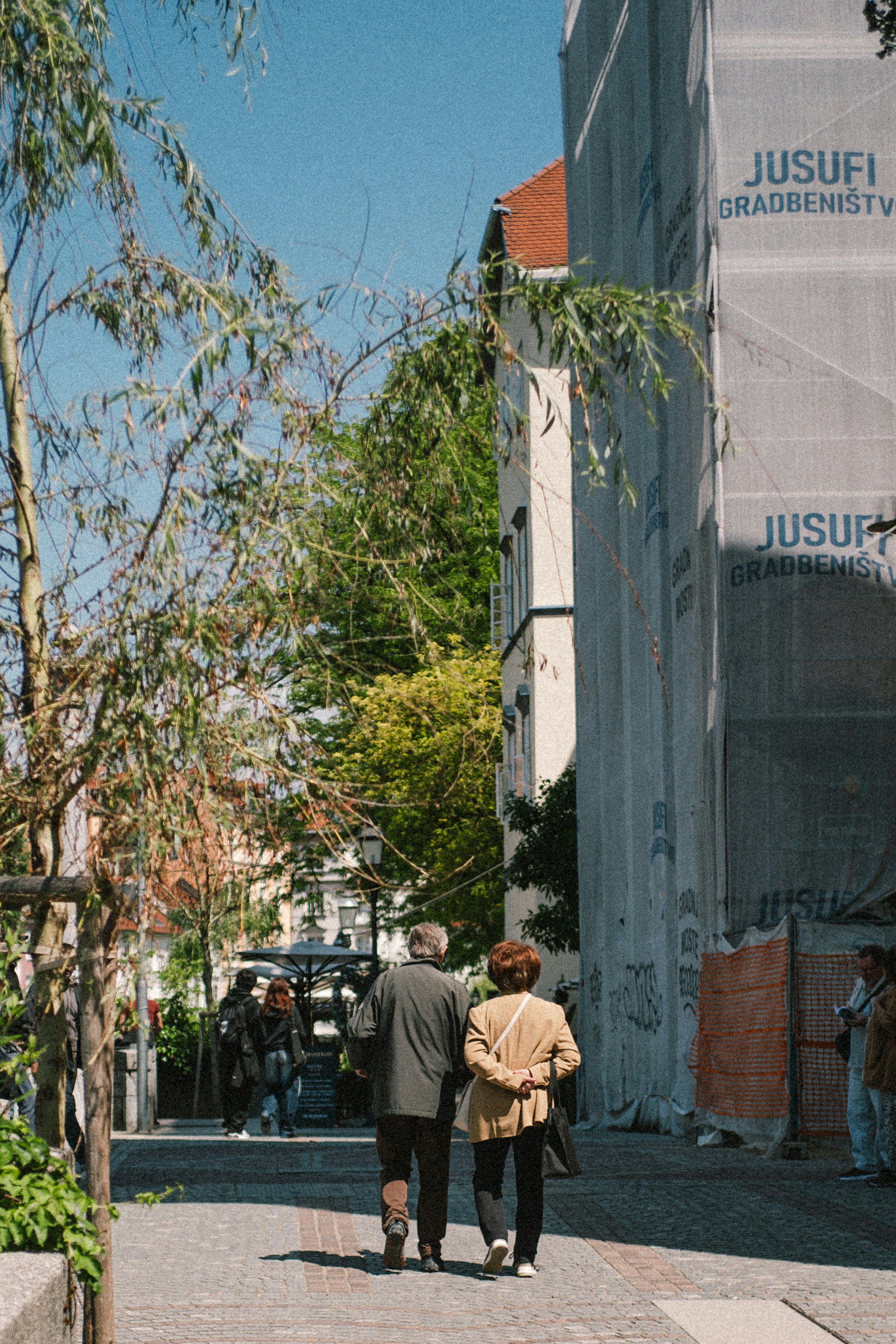 An elderly couple walks past trees and a construction building