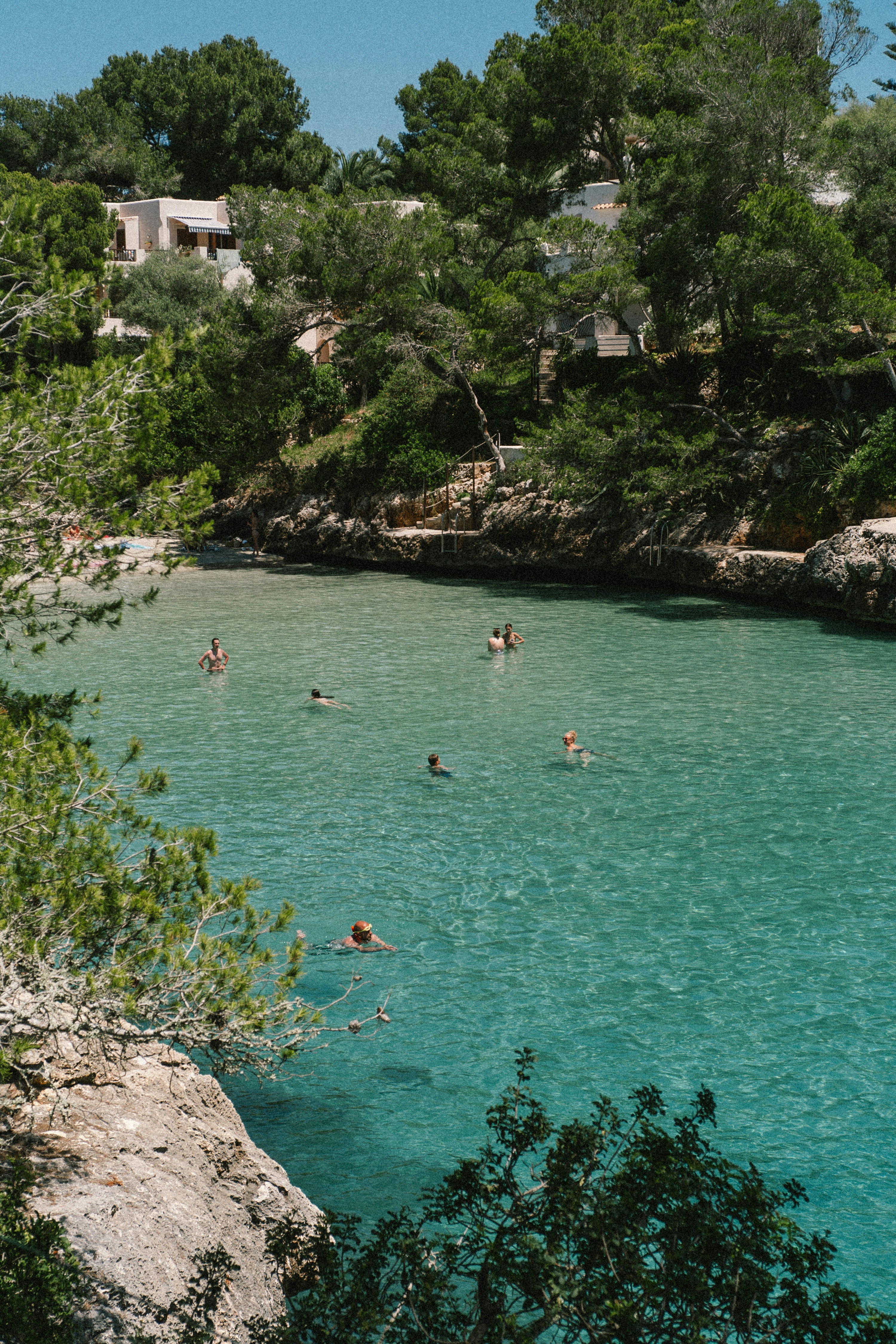 People swimming in clear turquoise water in a rocky cove.