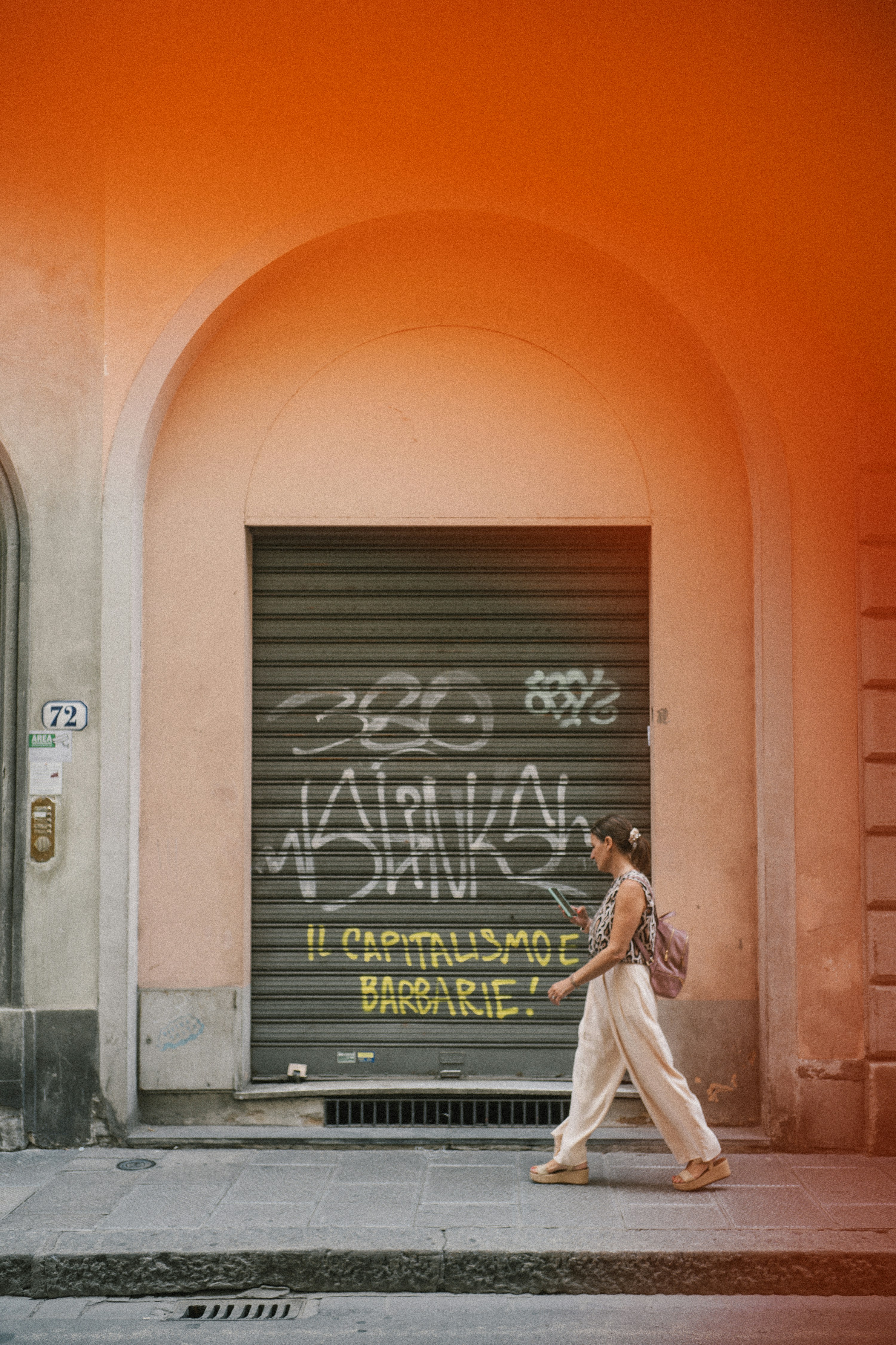 Una mujer pasa junto a la contraventana de un edificio cubierta de grafitis.