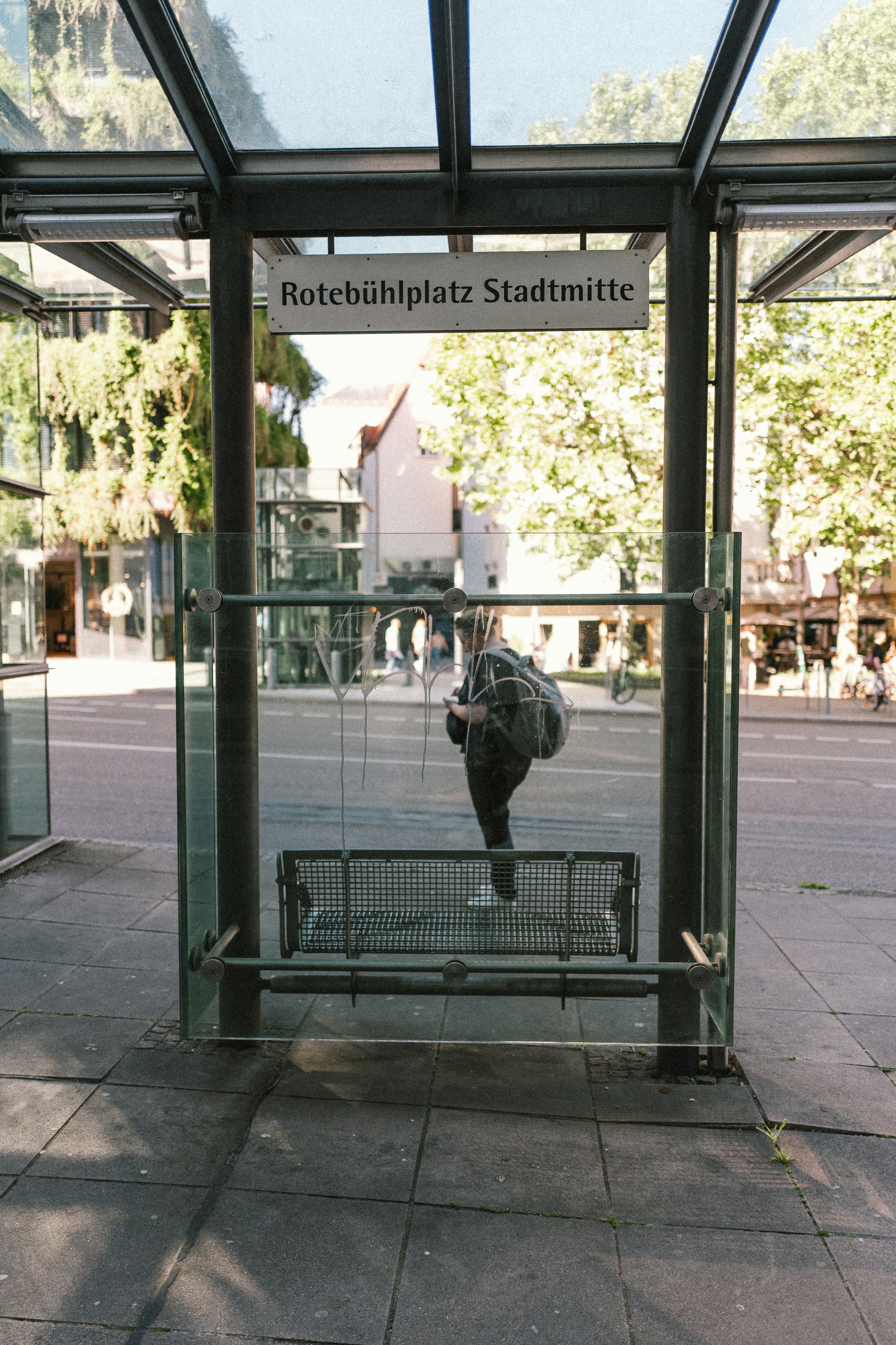 A person stands under a rotebühlplatz stadtmitte bus stop sign