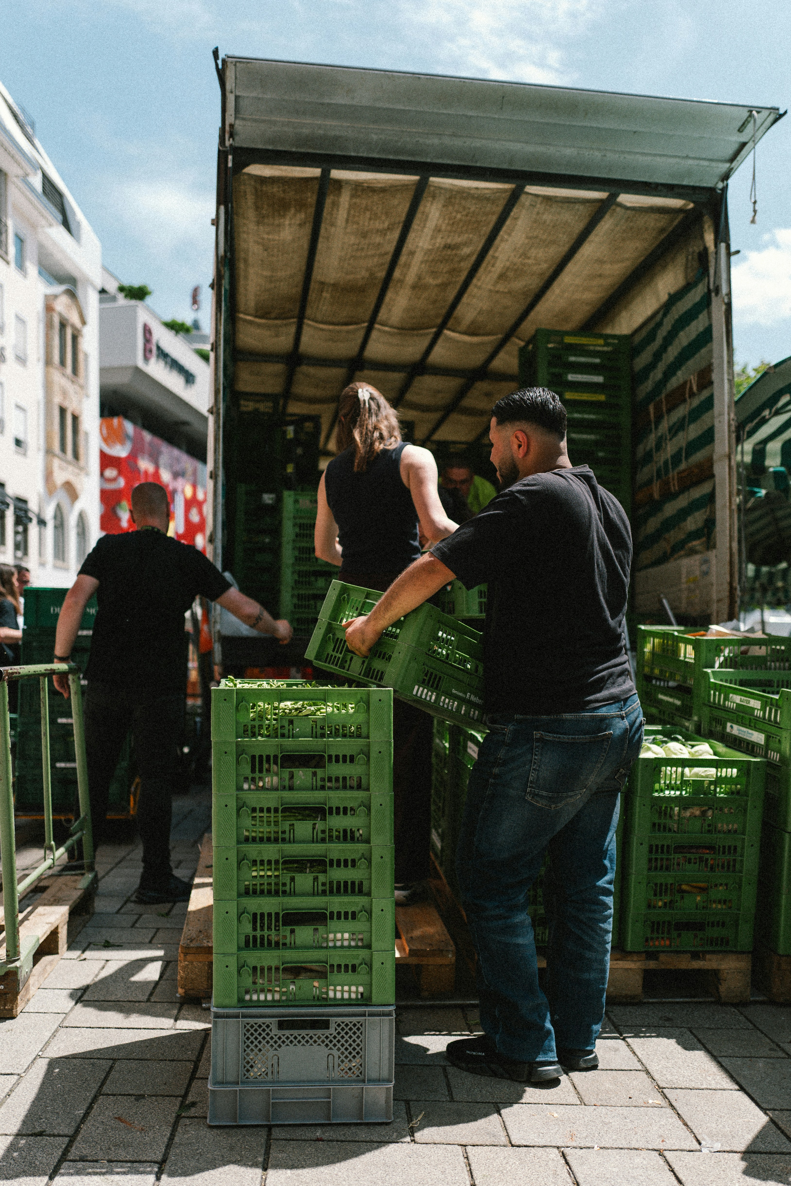 Kitchen staff unloading green produce crates from a delivery truck.