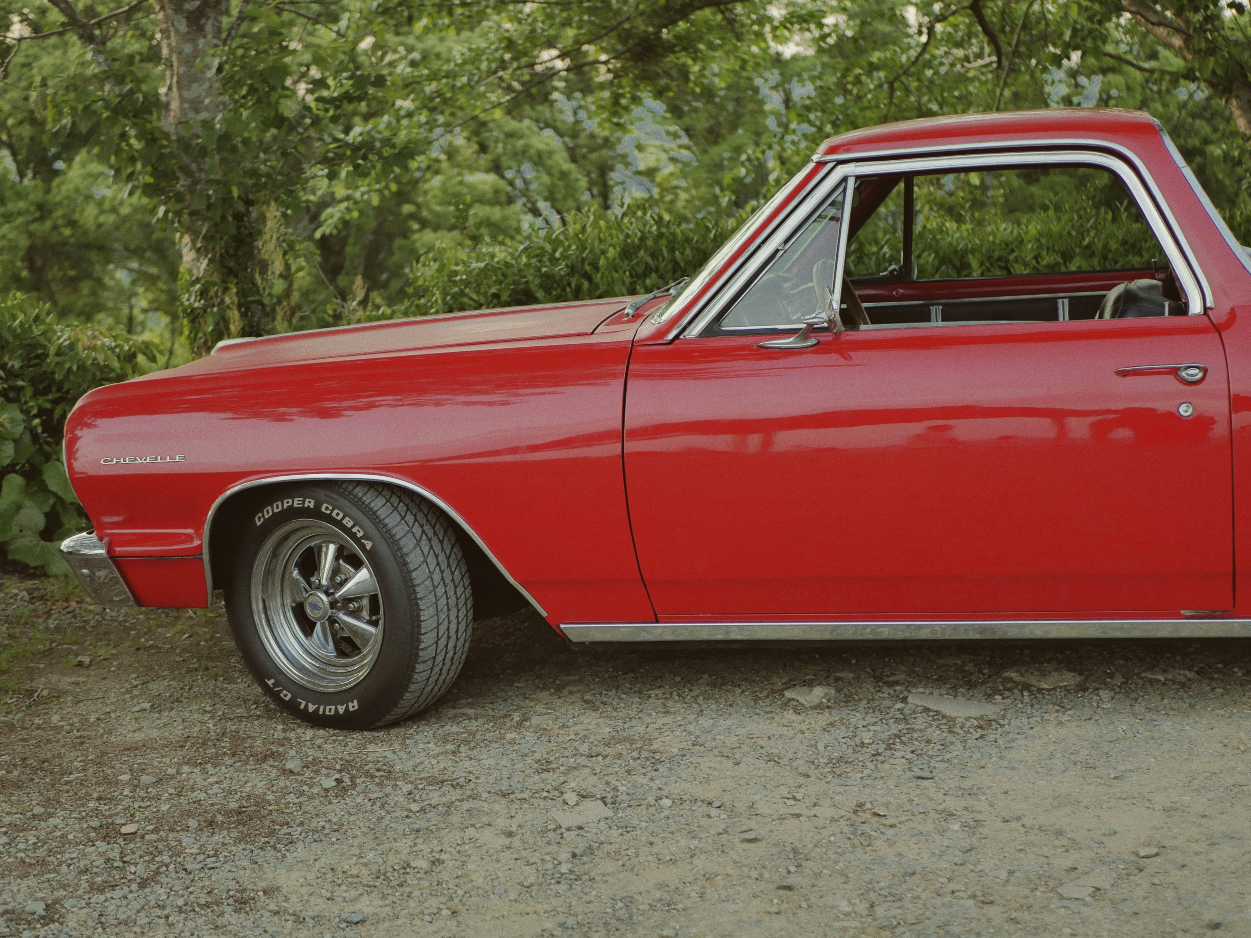 Side view of a red vintage car on dirt.