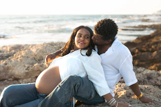 A pregnant woman and man relaxing on a rocky beach