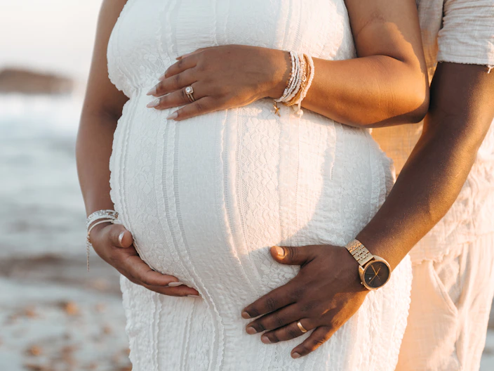 Man embracing pregnant woman's belly on a beach