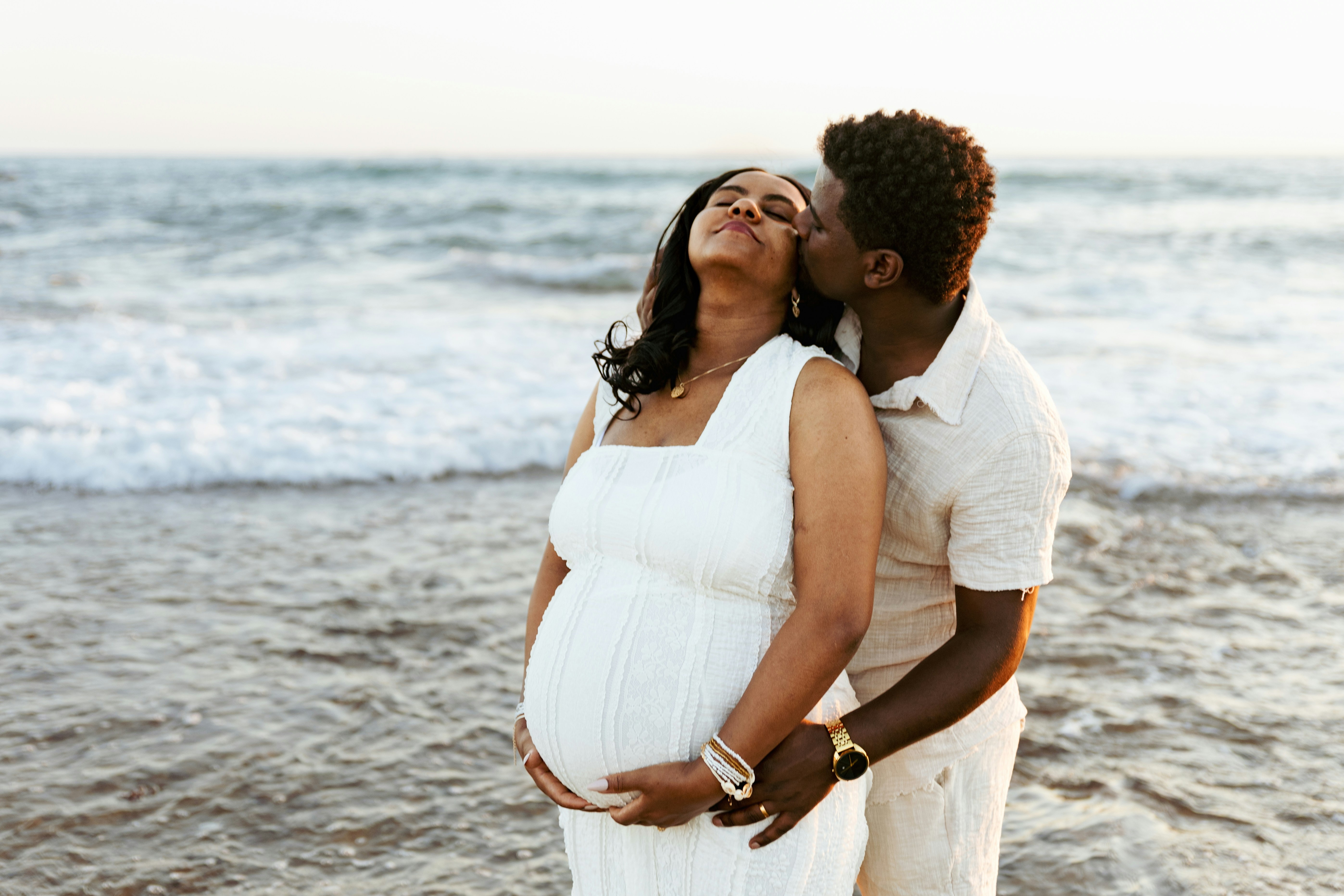 Pregnant couple embracing by the ocean at sunset