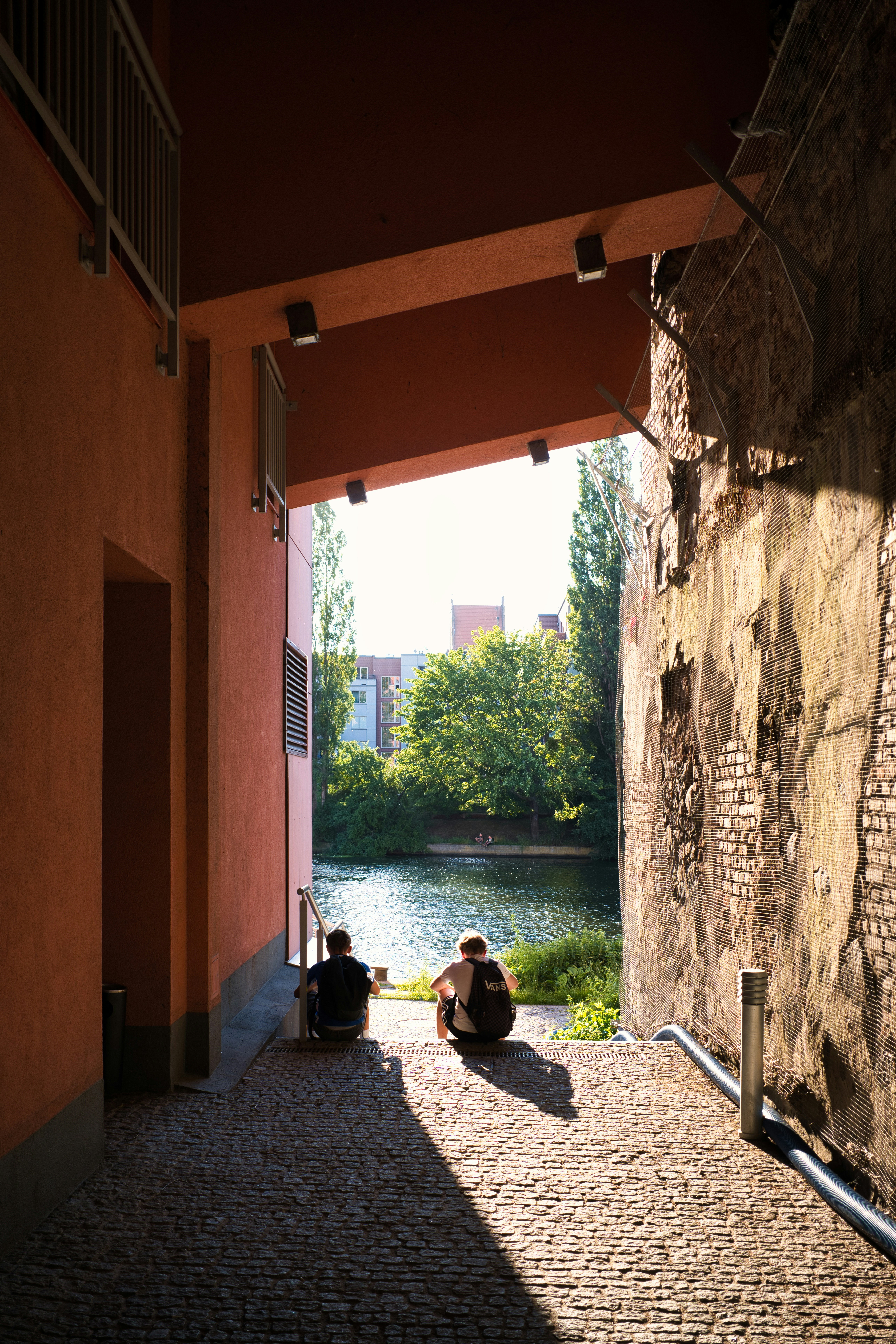 Two people sitting by a river framed by buildings.