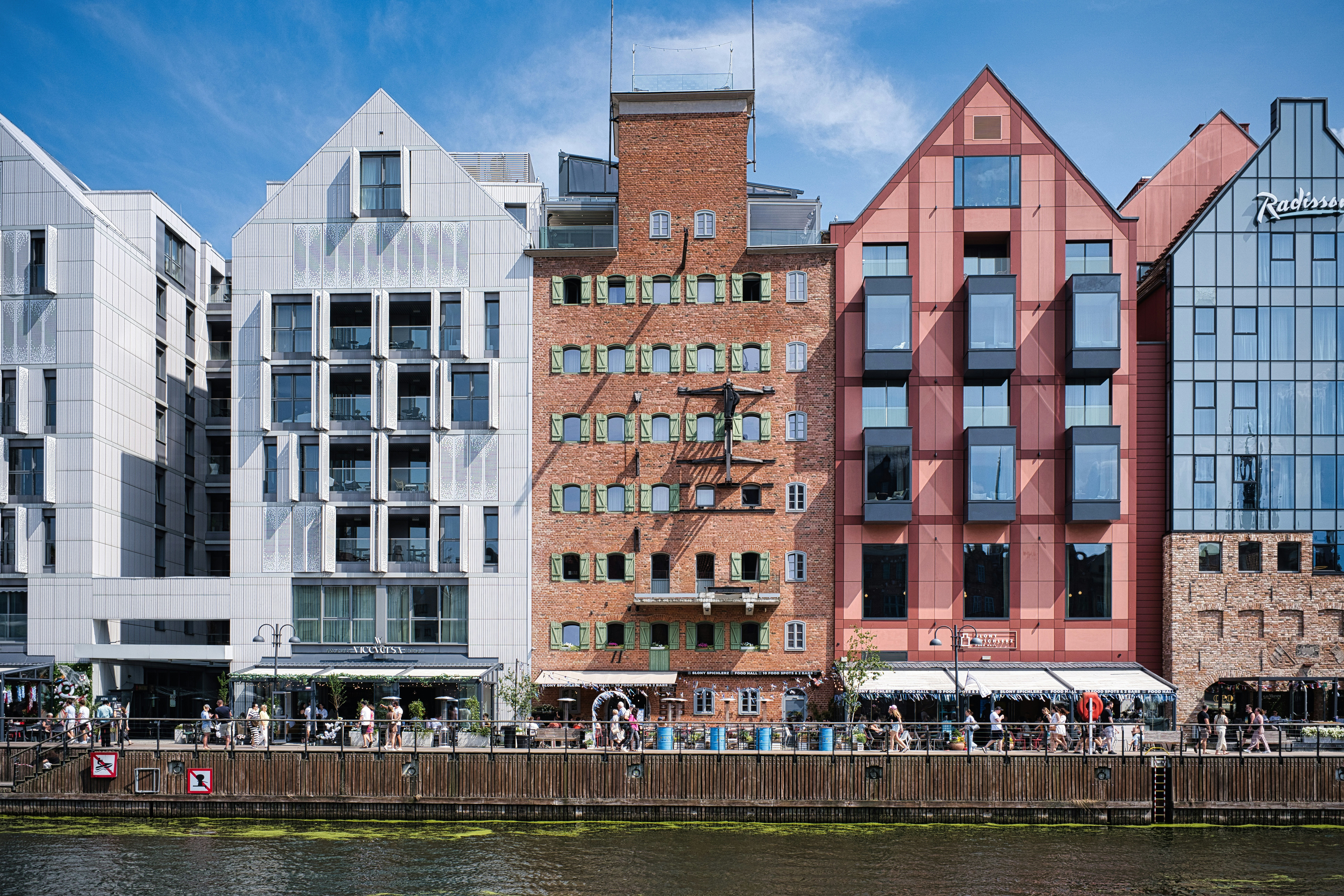 Colorful buildings line a waterfront with people walking by.