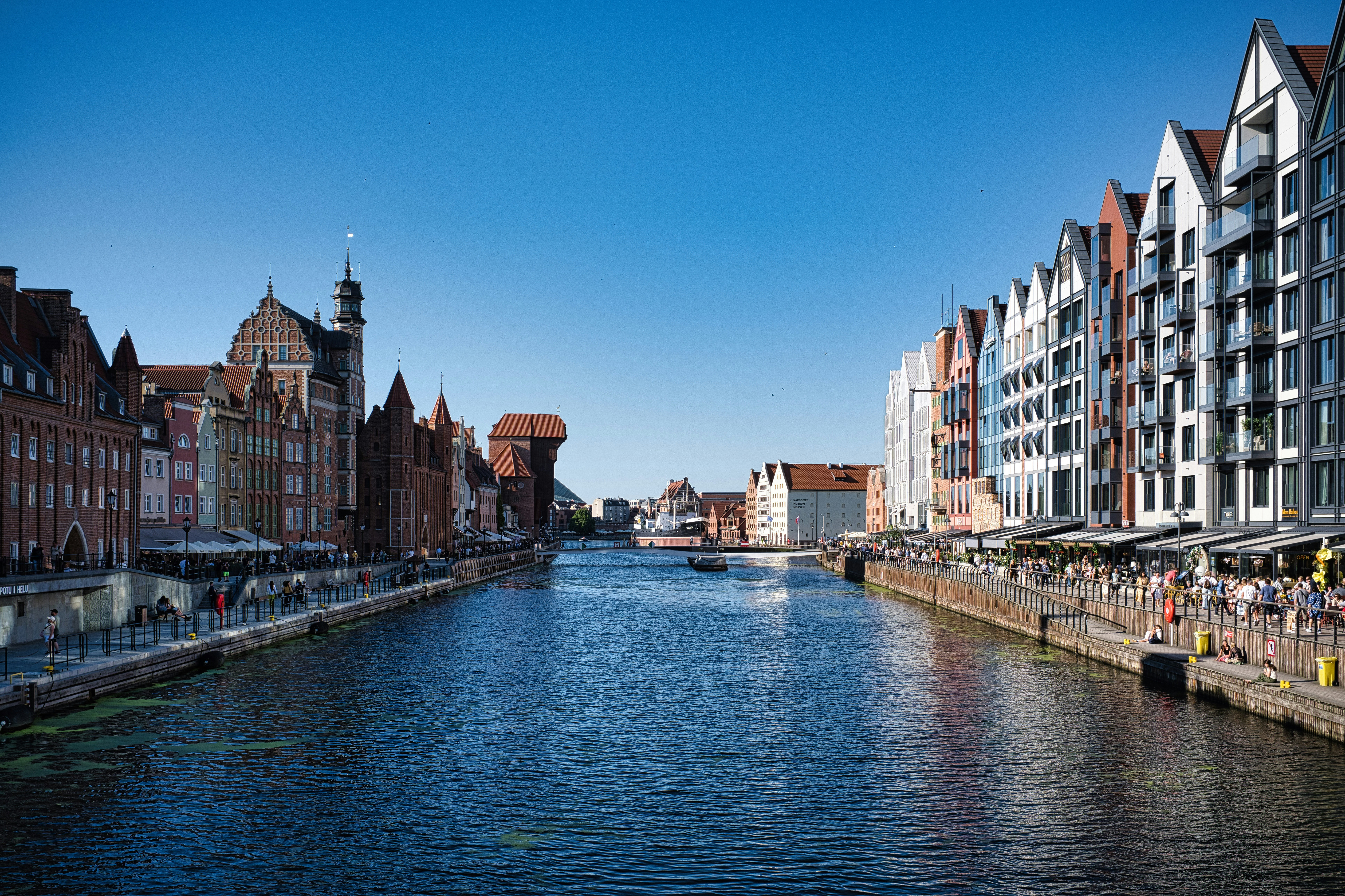 Historic buildings line a river under a clear blue sky.