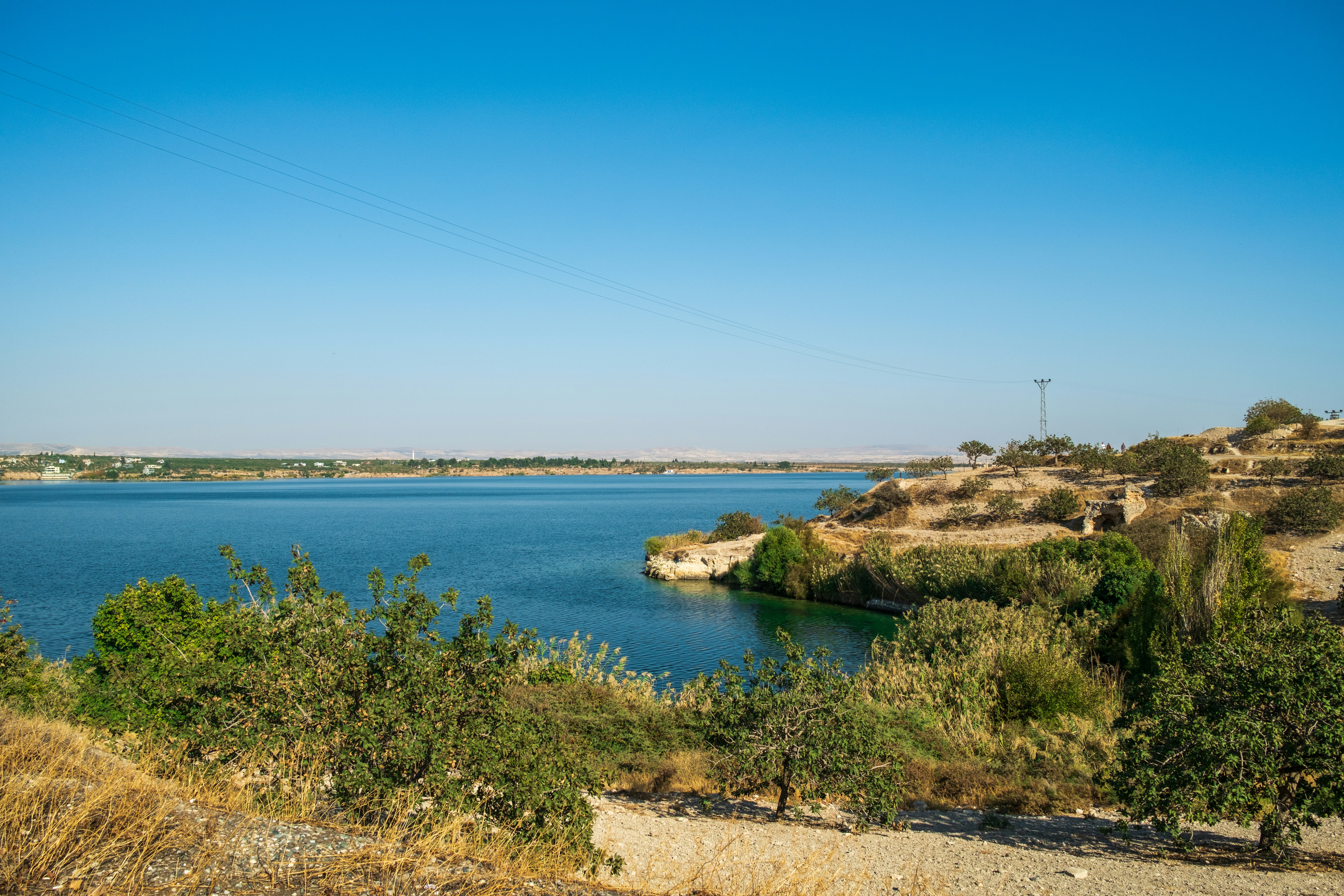 Expansive lake under clear blue sky with arid hills.