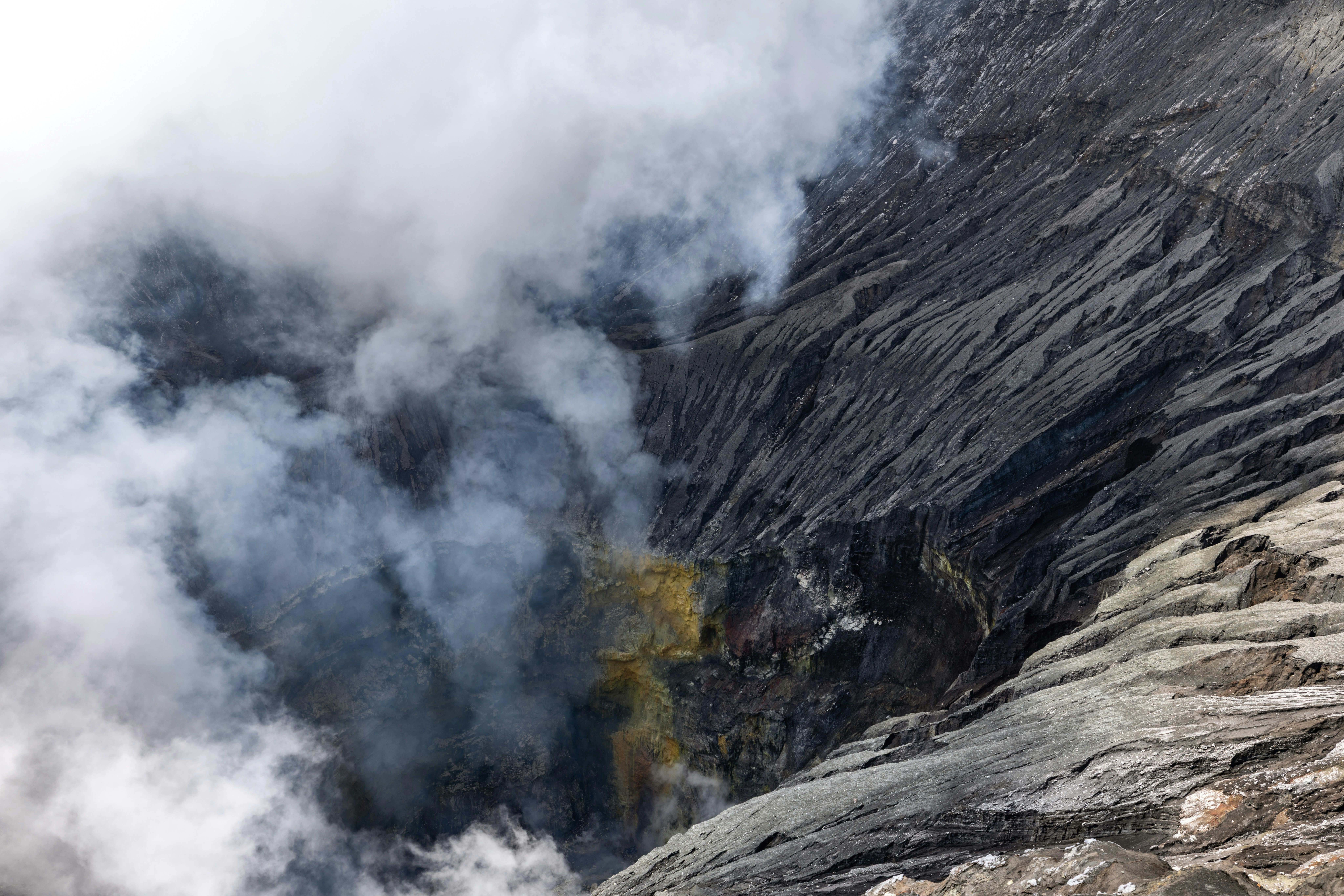 Thick smoke rises from a rocky volcanic crater.