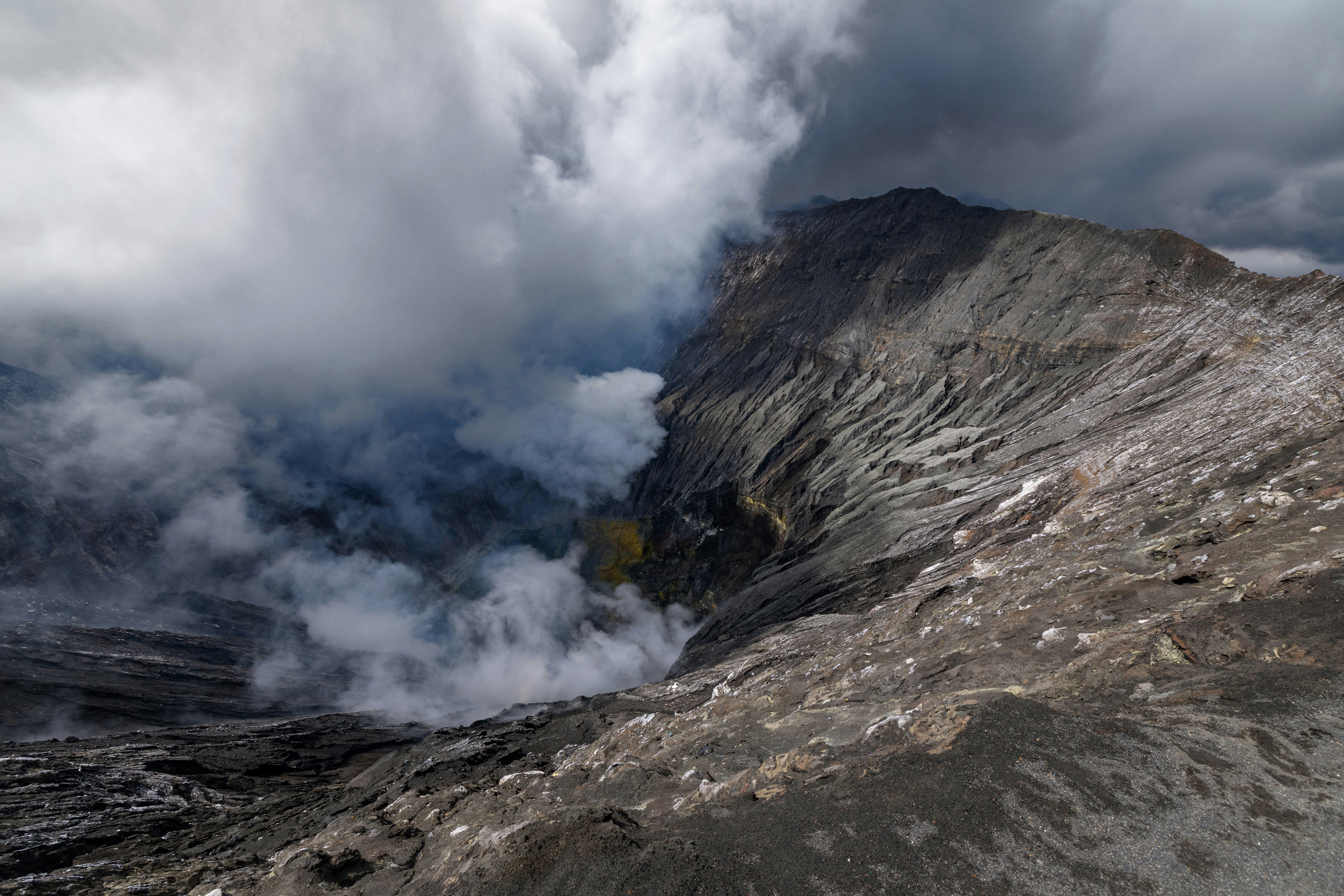 Volcanic crater with smoke and clouds under a dramatic sky.