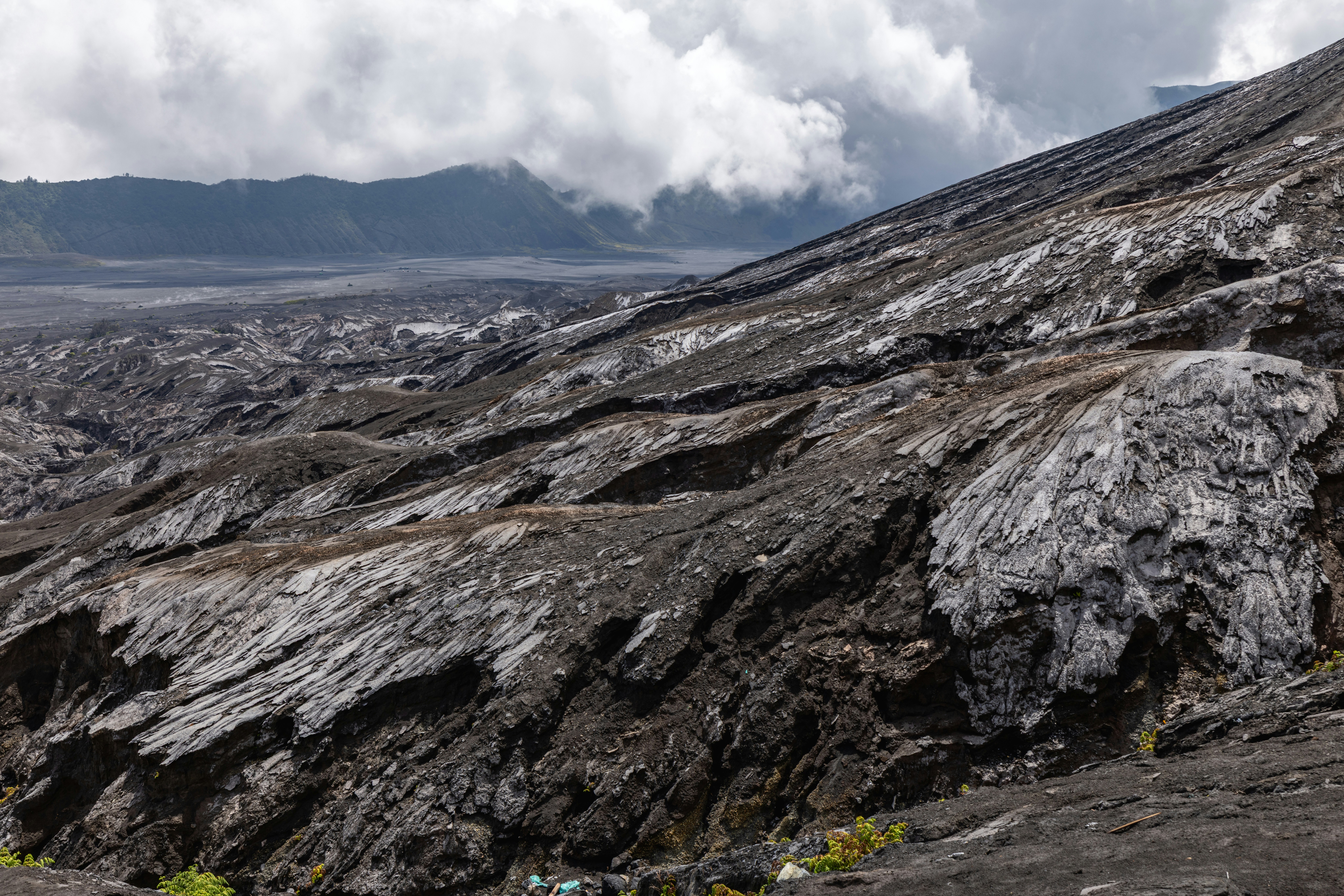 Rugged volcanic landscape with dark lava rocks and cloudy mountains.