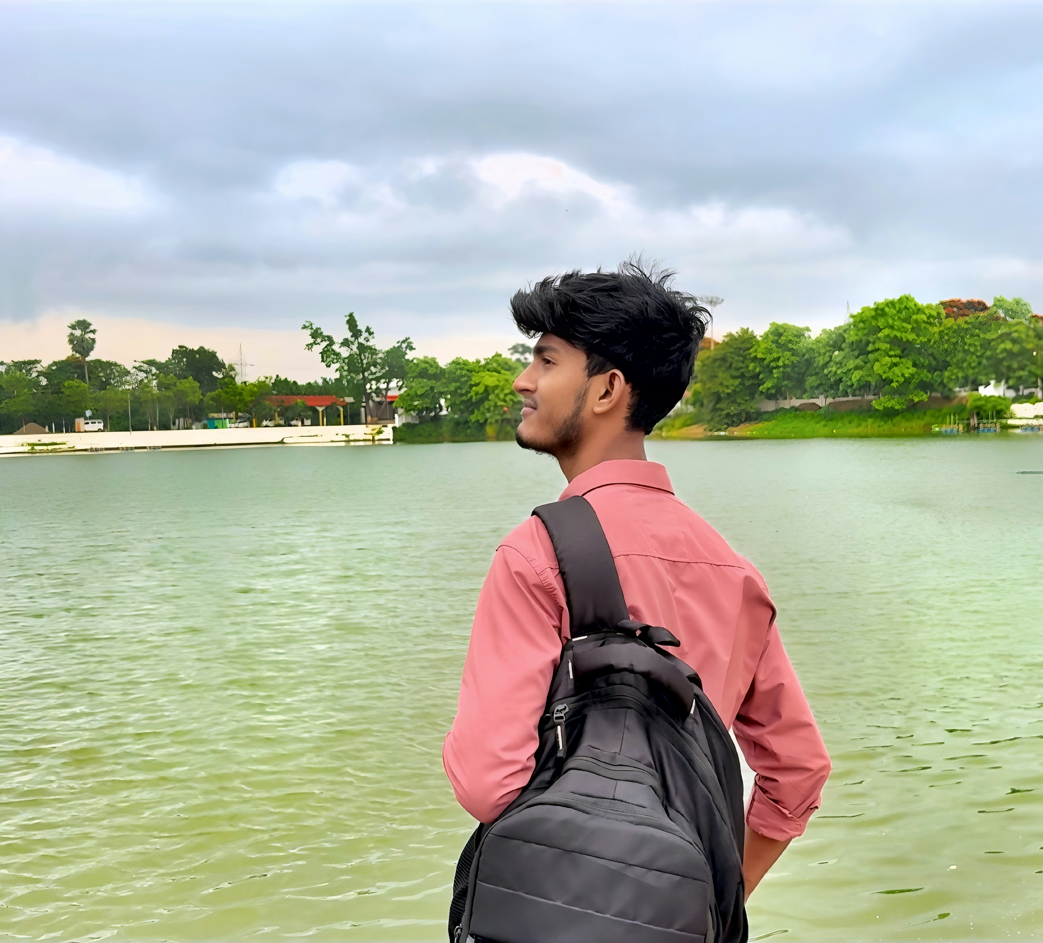 Jovem com mochila olhando para um lago verde.