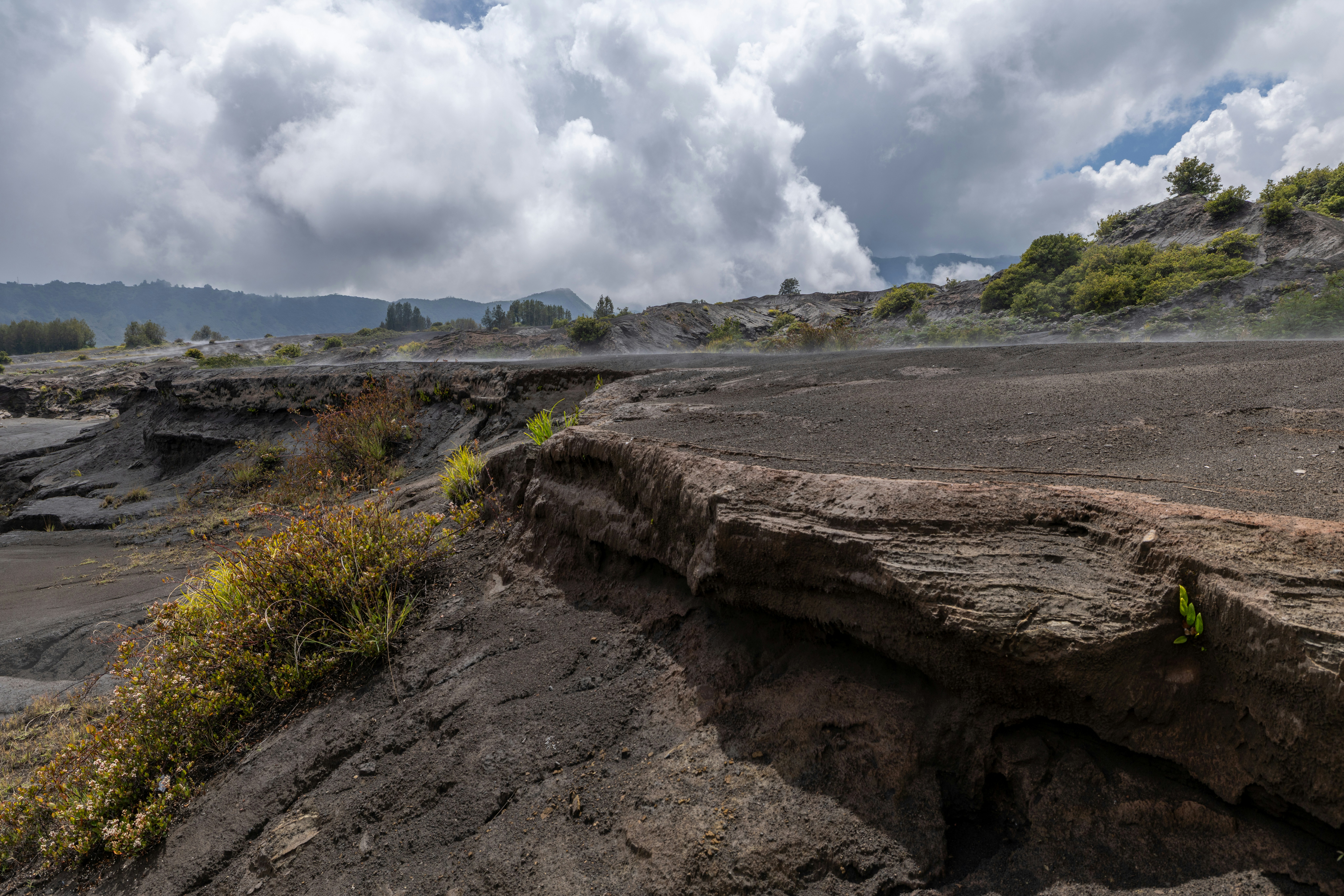 Volcanic landscape with steam rising under a cloudy sky.