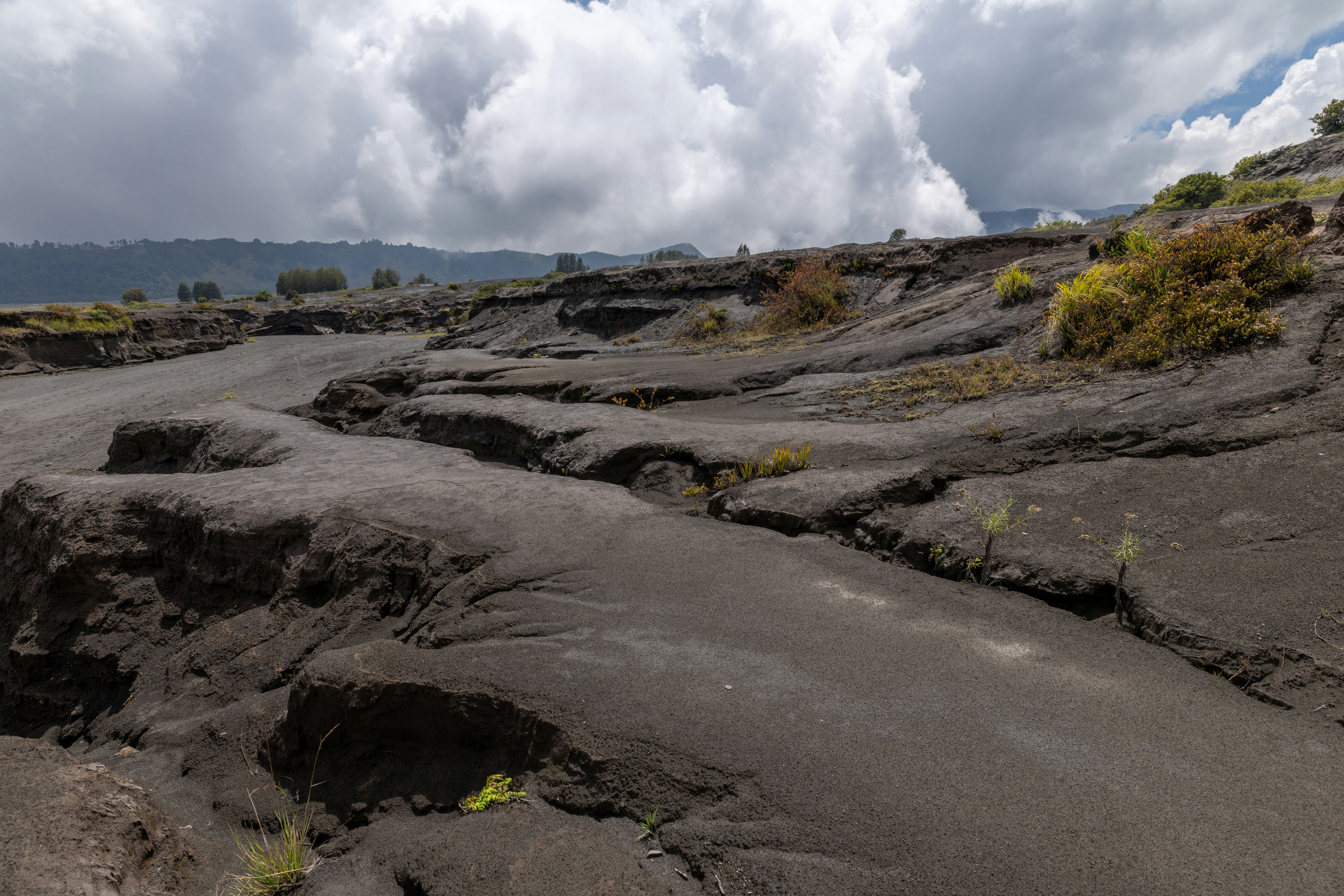 Rugged volcanic landscape with dark ash and distant clouds.